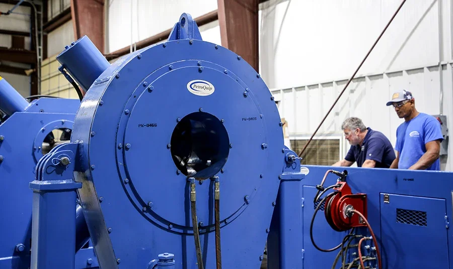 Two men working on large blue industrial machinery inside a factory or workshop.