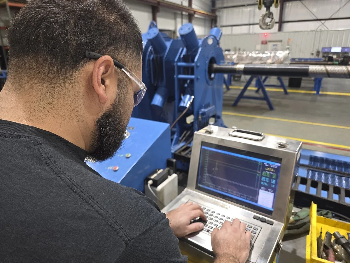 A PetroQuip team member with safety glasses and a beard working on industrial equipment setting, with blue machinery and equipment in the background.