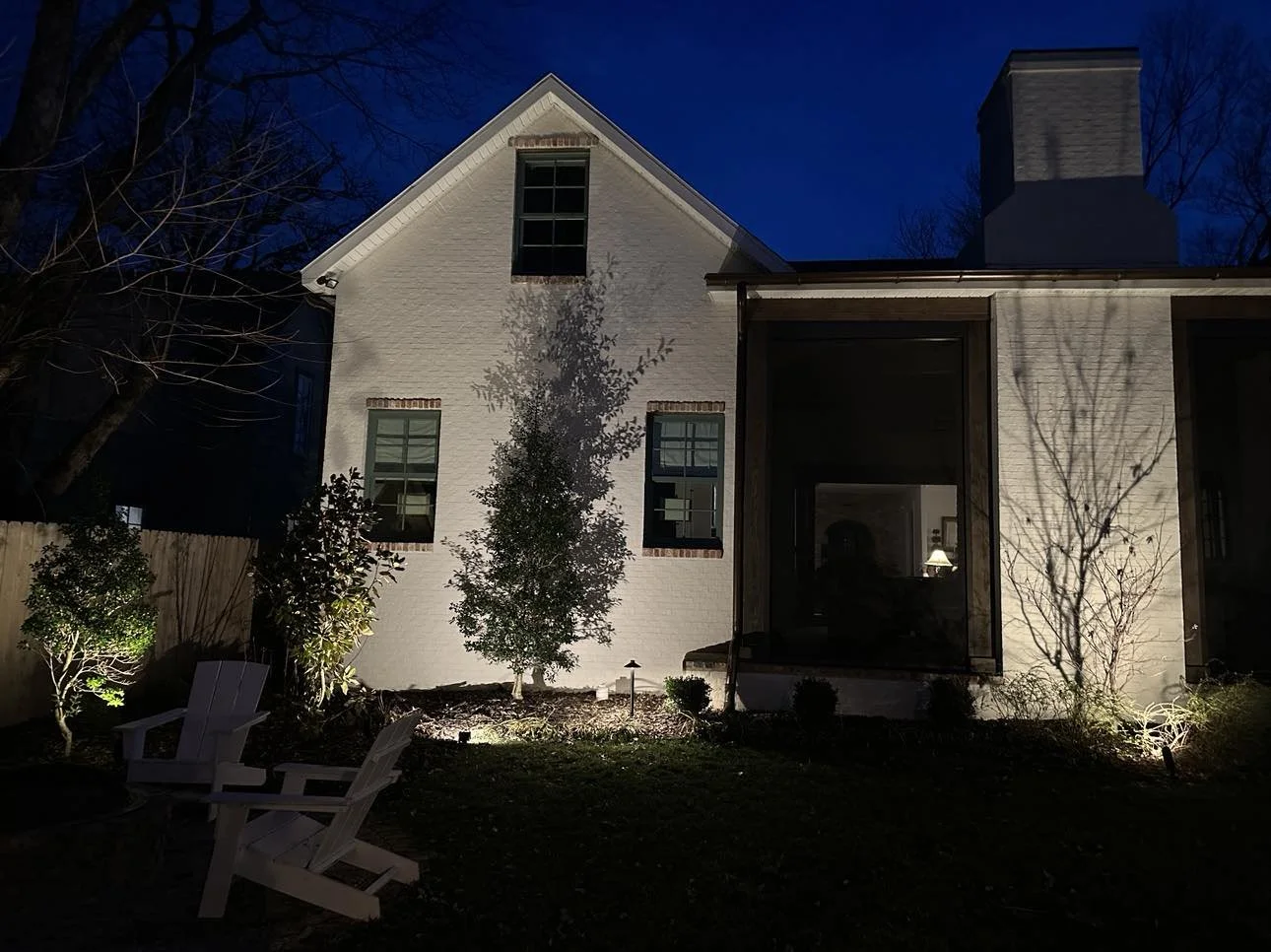 White farmhouse style home with LED architectural uplighting and front porch at night in Rogers Arkansas.jpg