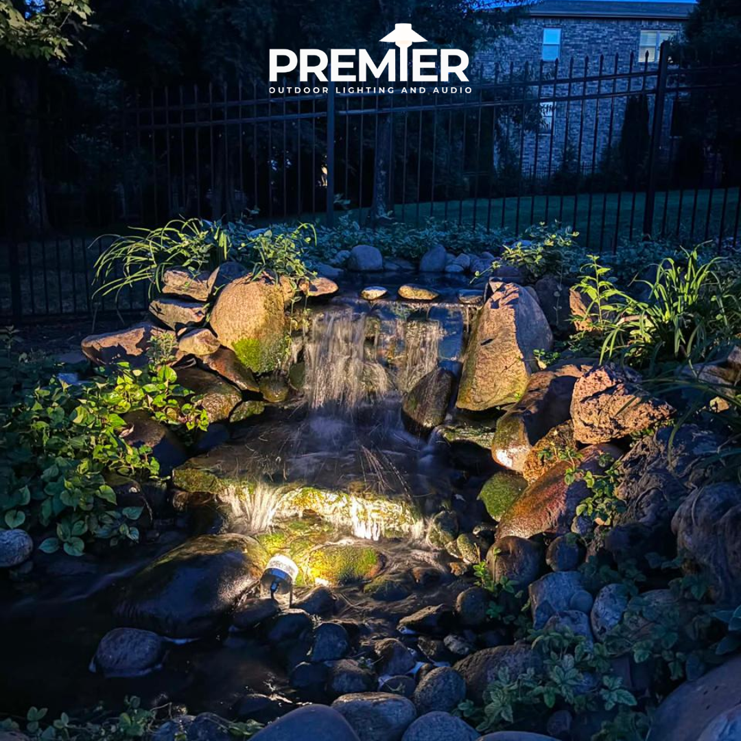 Backyard koi pond with an illuminated waterfall and underwater uplighting at night in Northwest Arkansas