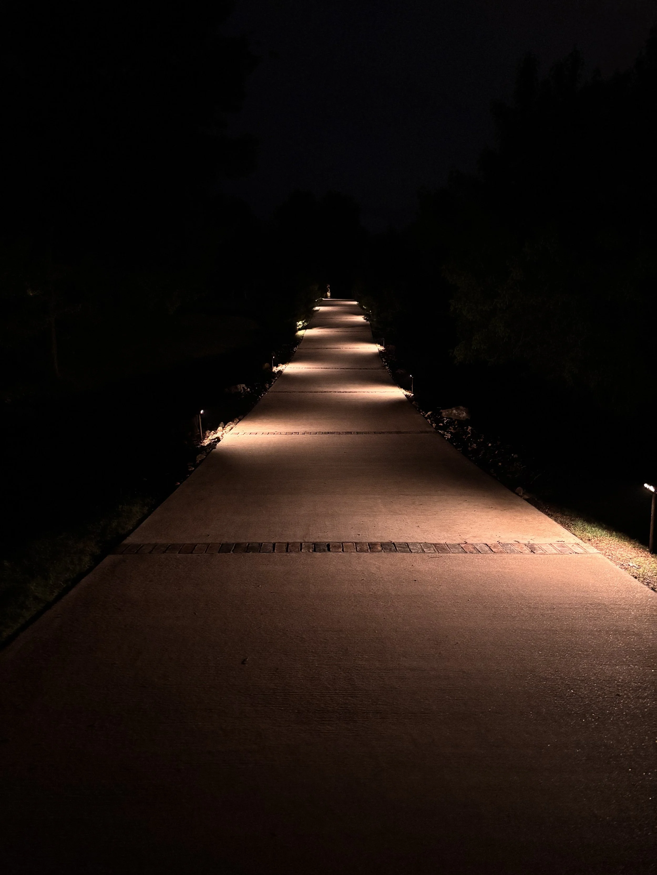 Long walkway illuminated by landscape path lights at night creating dramatic perspective.jpeg