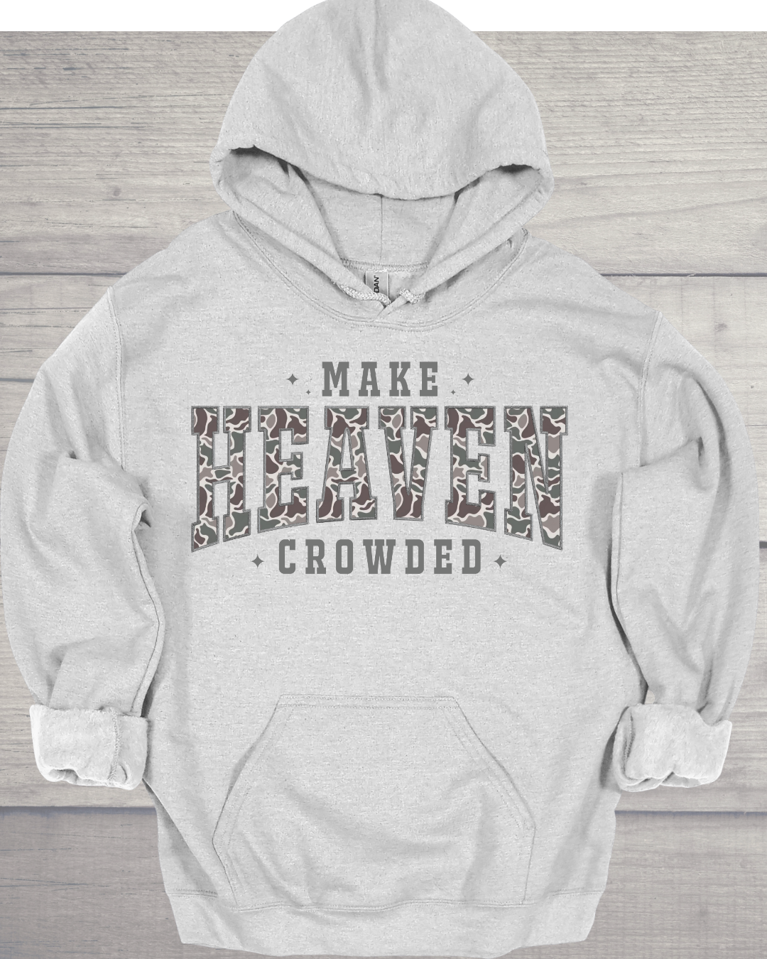 Light gray hoodie with the words 'Make Heaven Crowded' printed on it, with 'Heaven' in a large, camouflage-patterned font, laid flat on a wooden surface.