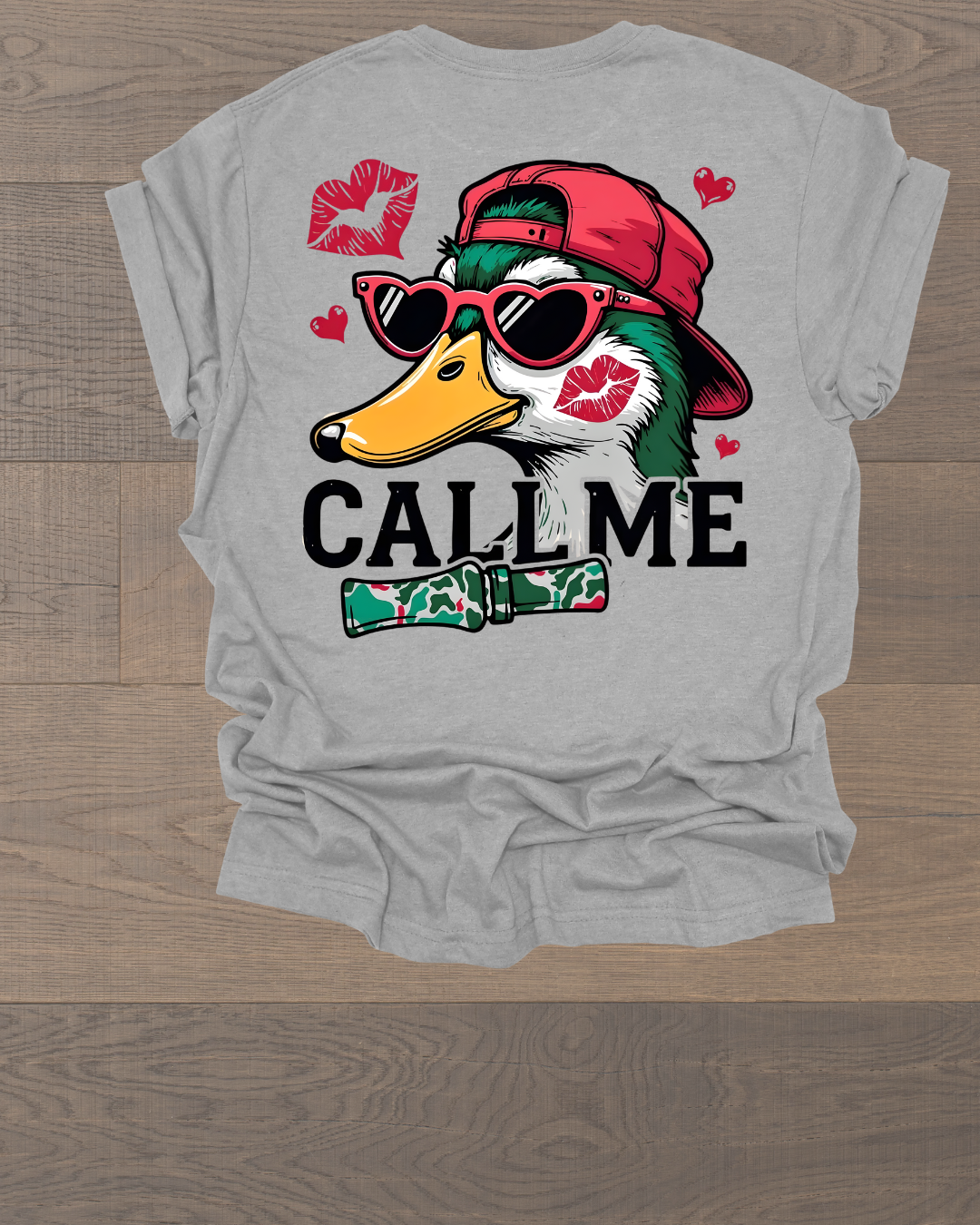 Gray T-shirt with a graphic of a duck wearing red sunglasses and a red cap, surrounded by red hearts and lips. The word 'CALL ME' is printed below the duck with a camo-patterned tie.