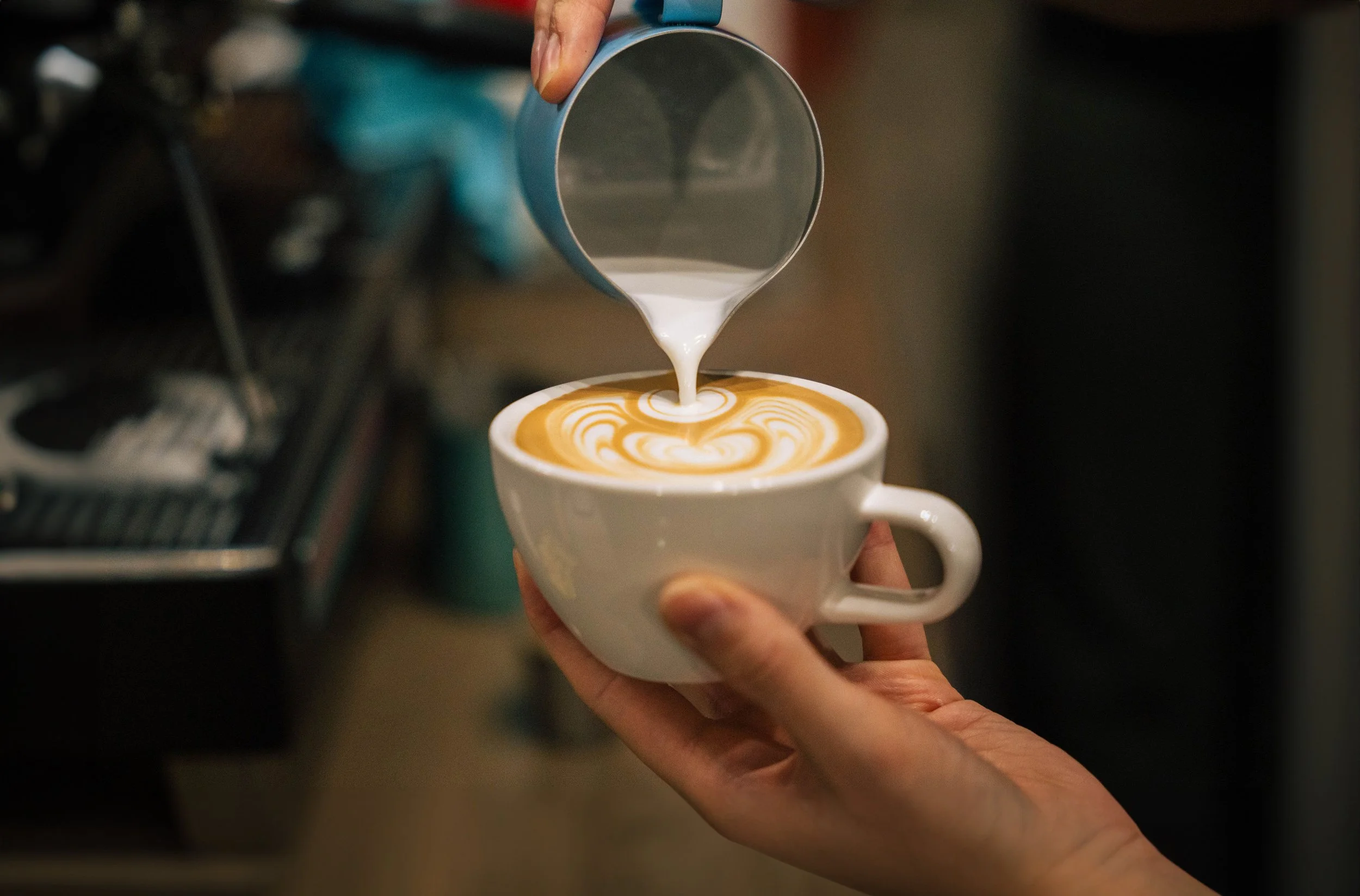 A young man in a gray polo shirt and beige pants sitting on a cushioned bench against a plain beige wall, casting a shadow.