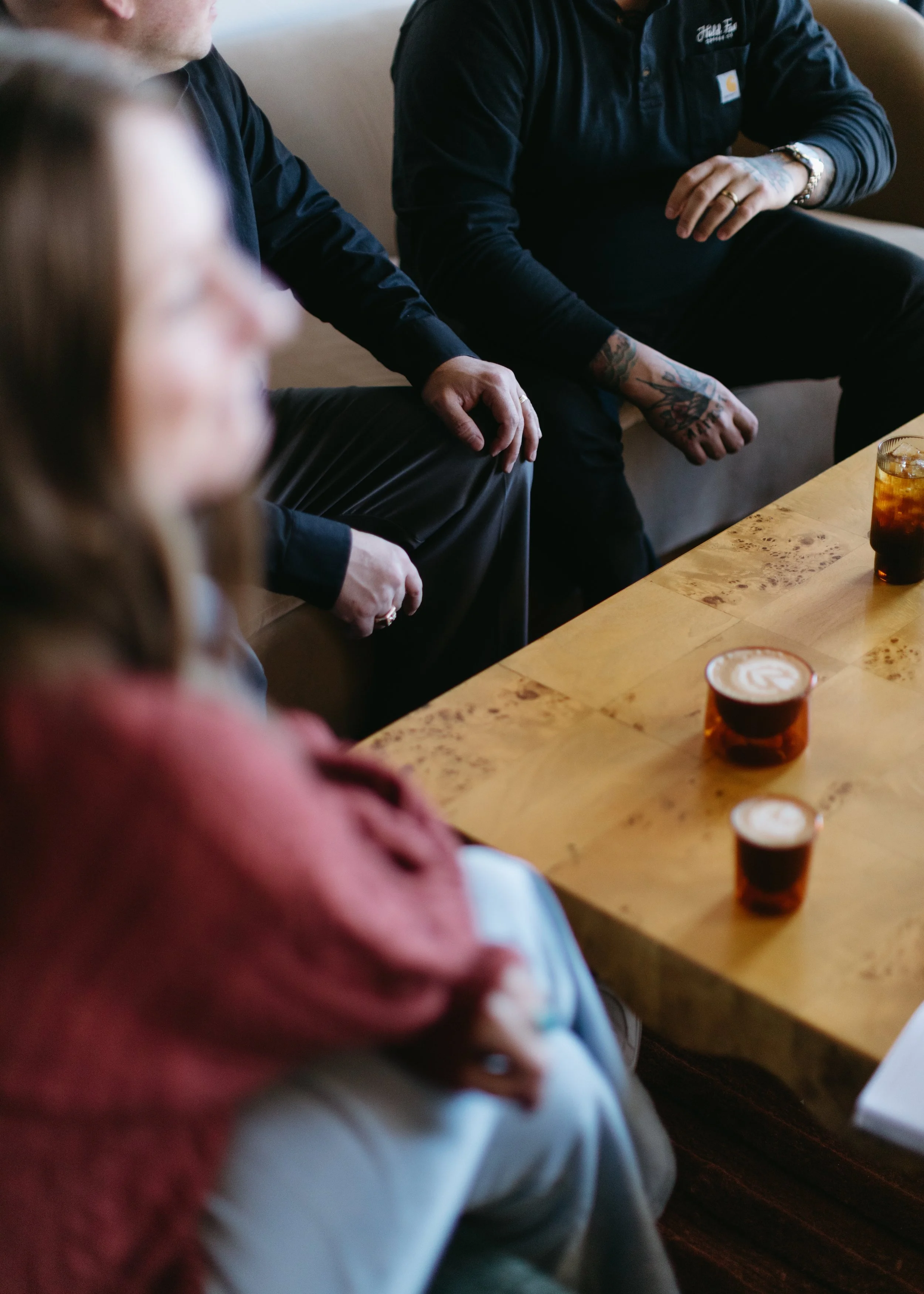 People sitting around a wooden table with drinks, engaging in conversation.