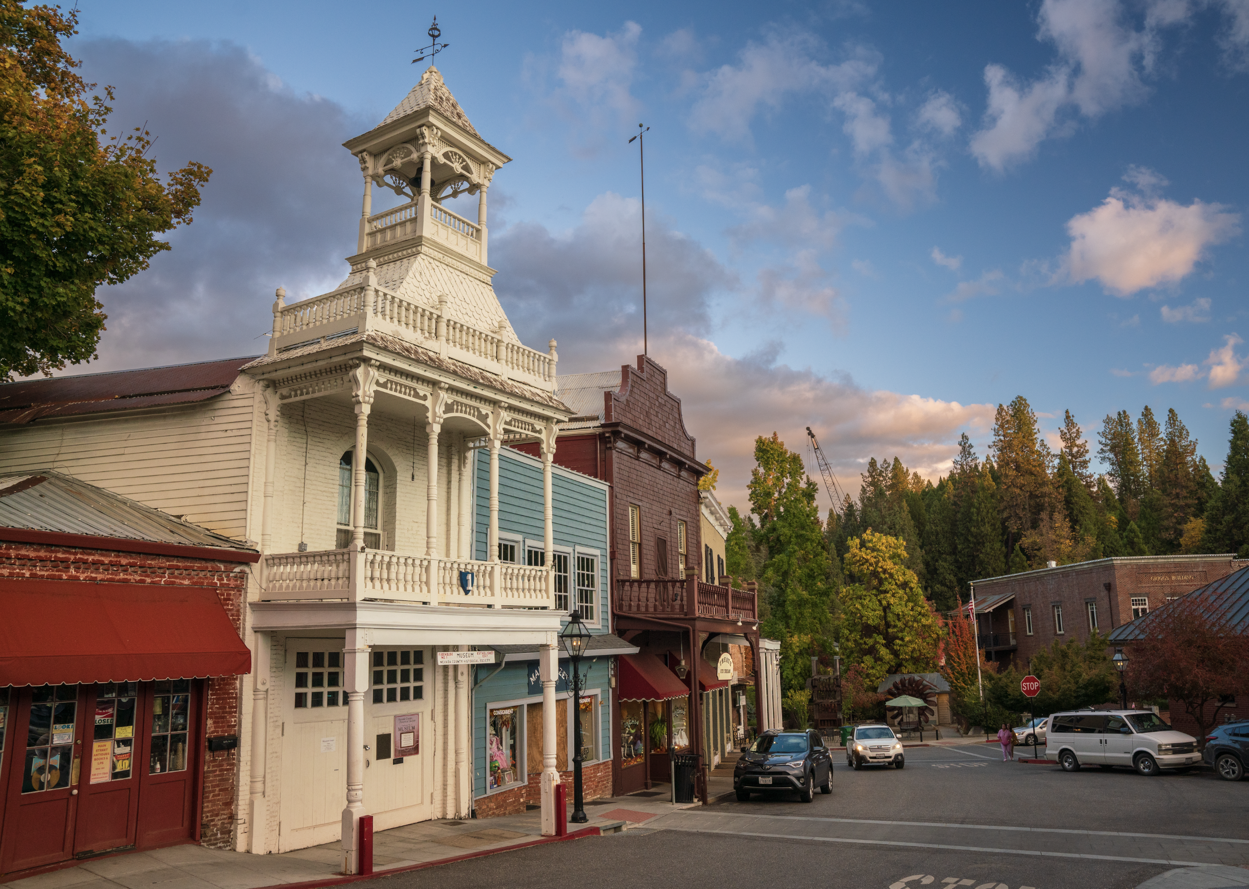 A small town street with historic buildings, including a white Victorian-style building with a tower, under a partly cloudy sky during dusk.