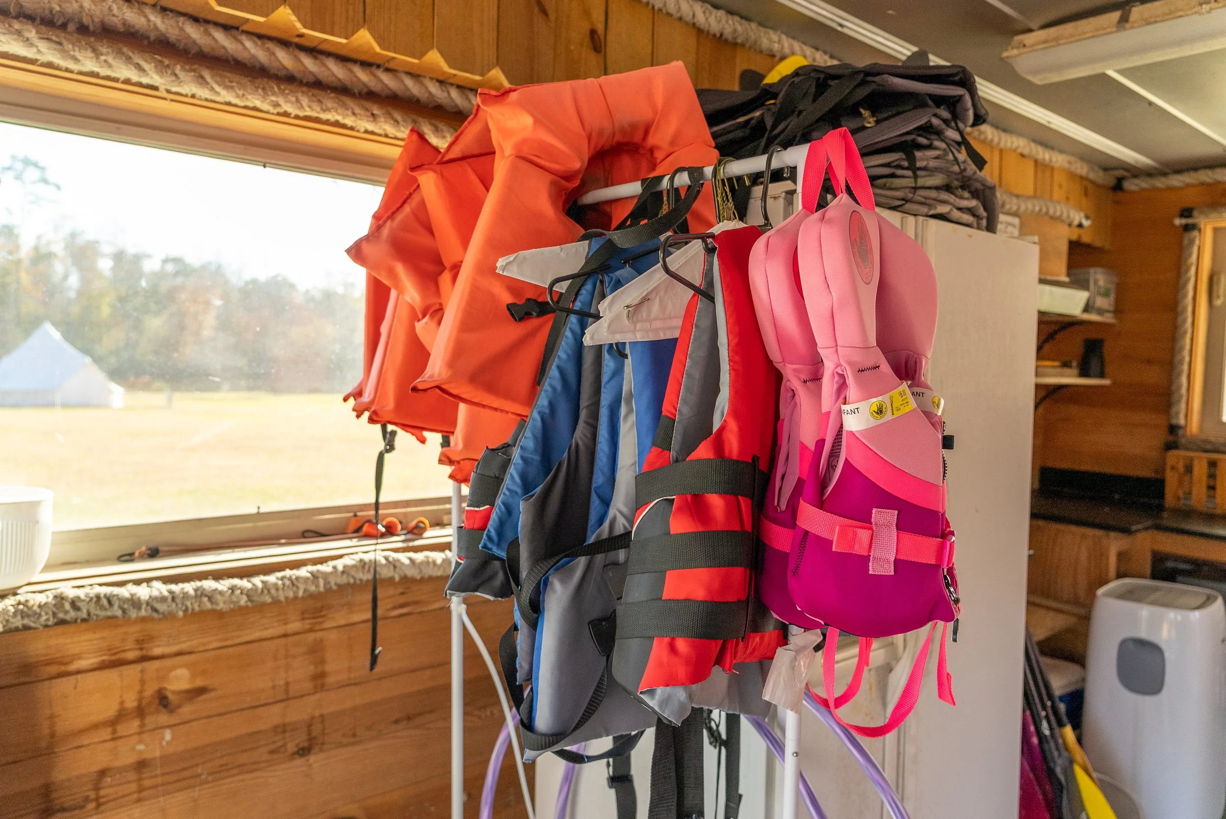 White bell tent pitched on grassy riverside area near Calcasieu River, with outdoor seating and trees, representing peaceful glamping accommodations at Bayou Glamping Co.