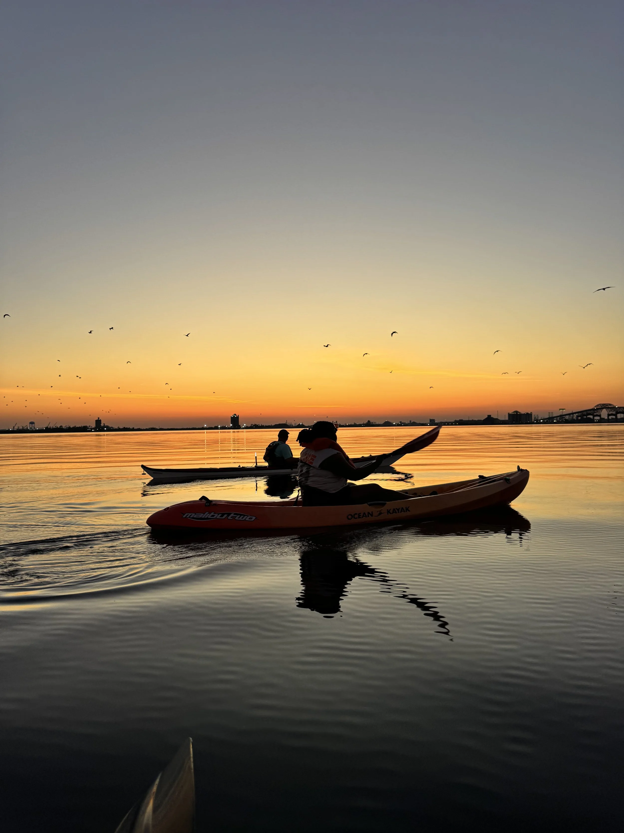 Two people sitting on wooden bench overlooking Calcasieu River, wearing sun hats and casual clothes, enjoying quiet nature views at Bayou Glamping Co.