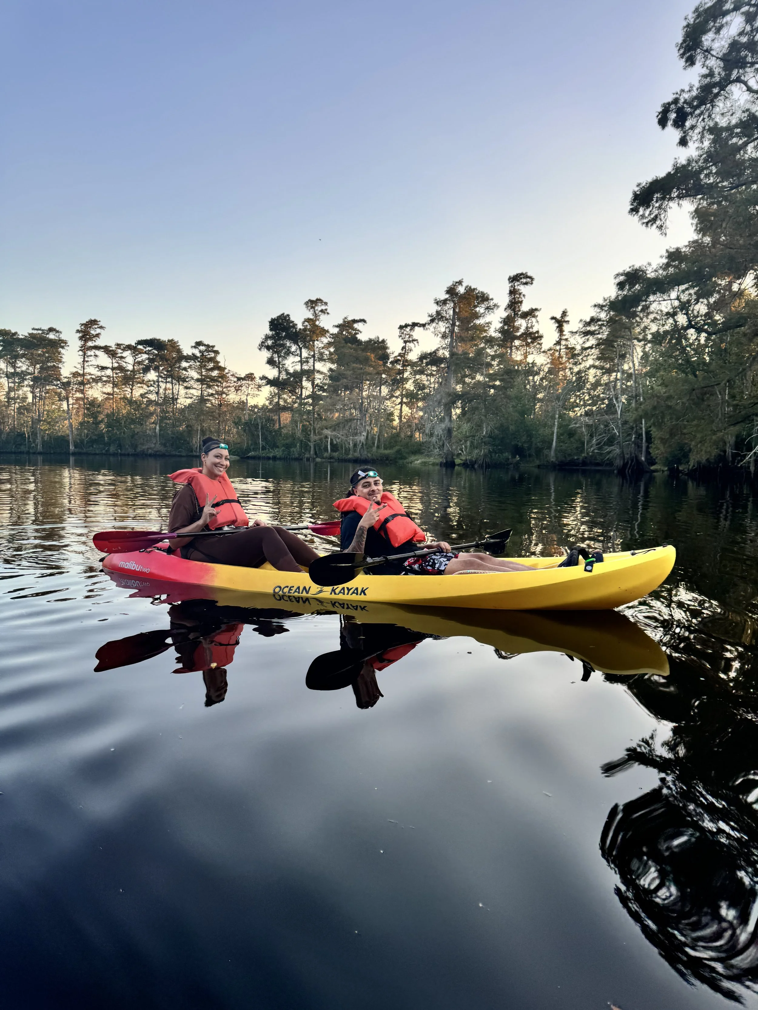Interior of the luxurious Riverside Deluxe Glamping Tent at Bayou Glamping Co. tent featuring two beds, wicker chairs with pillows, wooden table, potted plants, wine glasses, and natural decor creating cozy ambiance.