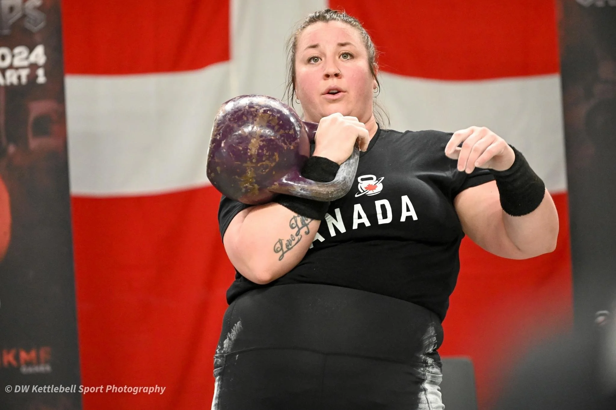 A woman lifting a kettlebell at a gym with a Canadian flag in the background.