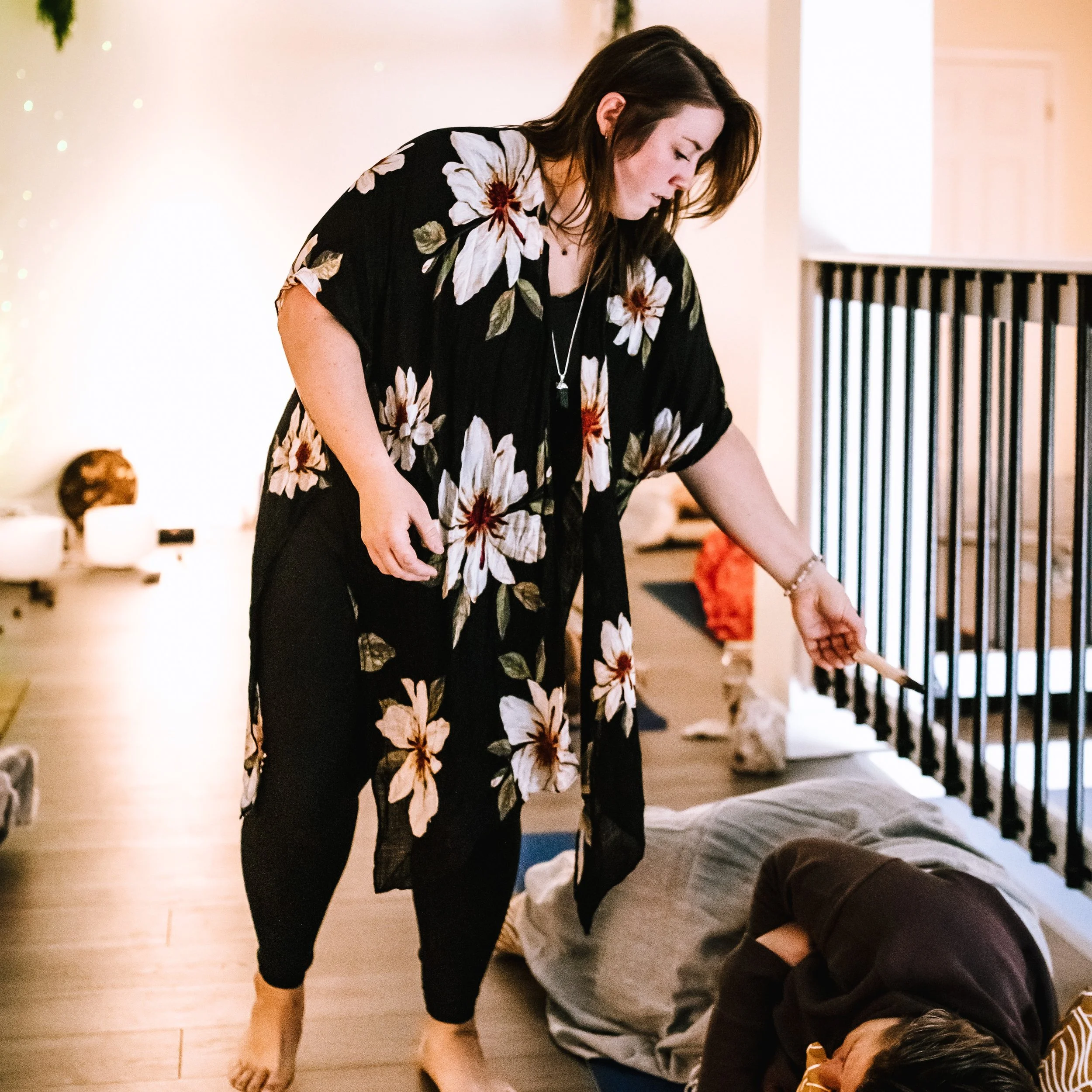 A woman in a floral dress is performing CPR on a person lying face down on the floor. The scene appears to be indoors, possibly in a home setting.