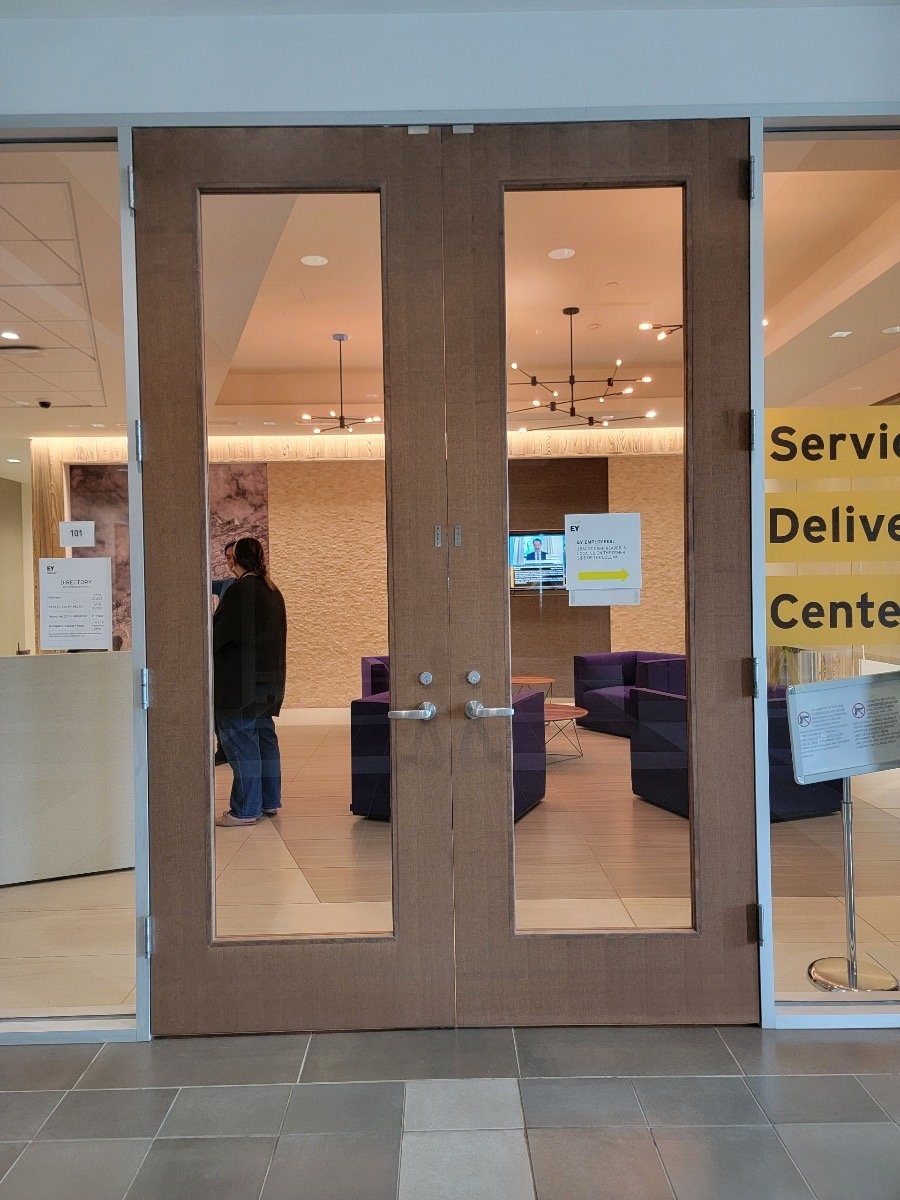 Entrance to a service delivery center with glass doors, revealing an interior with purple chairs, a modern design, and a person standing inside. Signs and directories are displayed near the entrance.