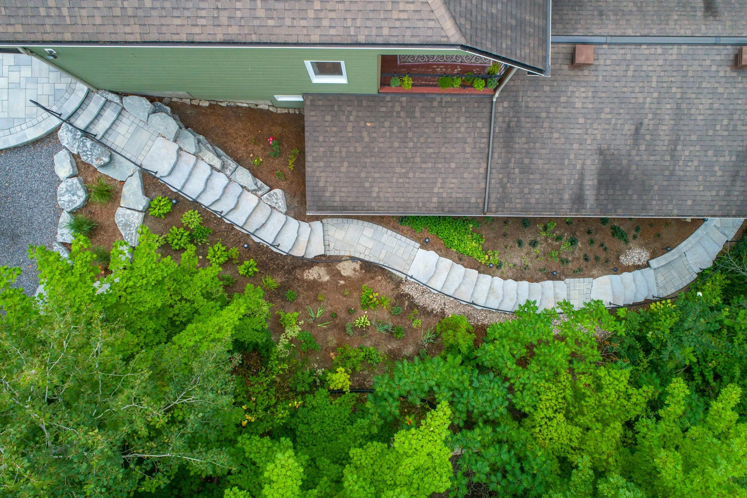 Aerial view of a backyard with a curved stone pathway, garden, and house with brown roof and green siding.