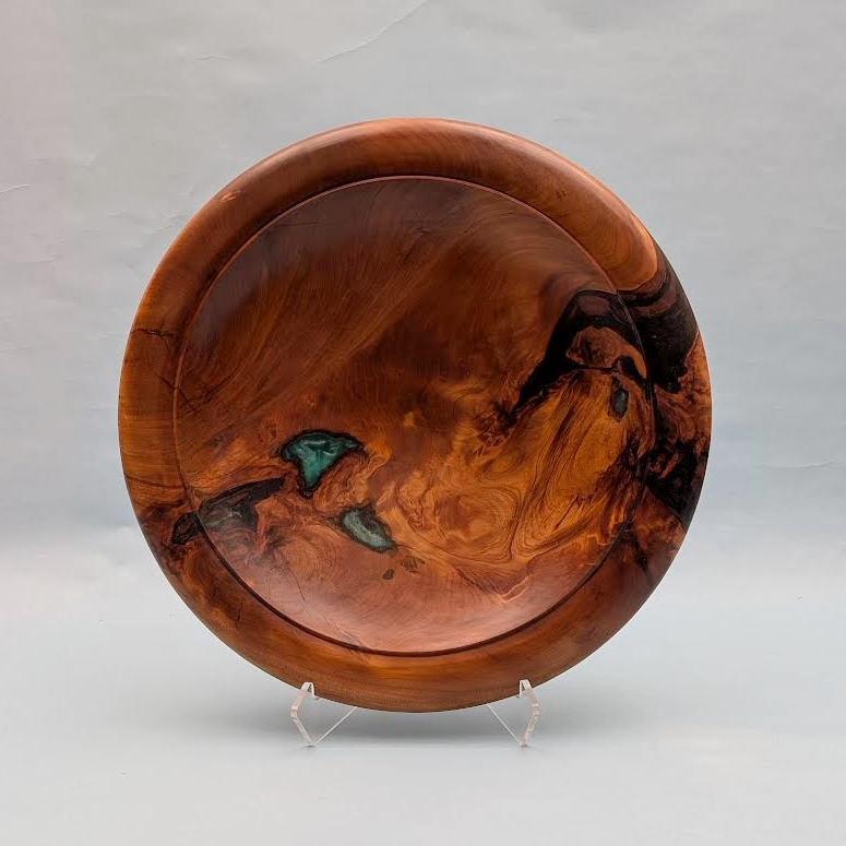 A round wooden Kauri bowl with natural grain patterns and dark accents, displayed on a clear stand against a light background.