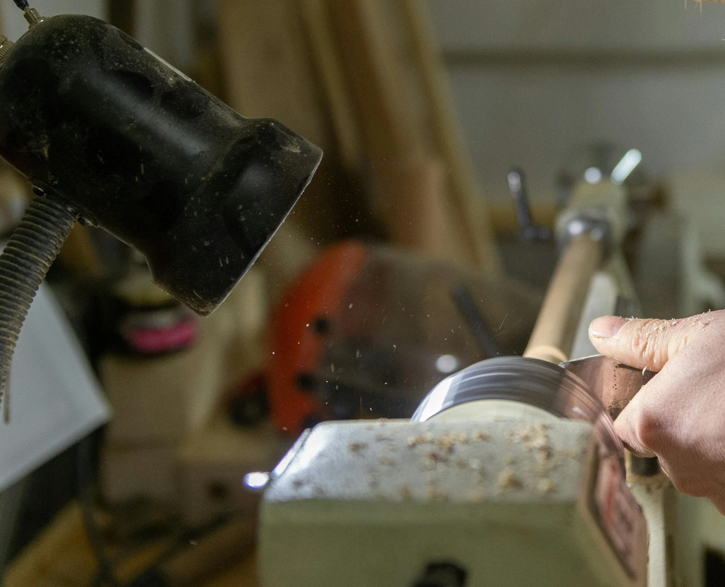 A person shaping wood on a lathe, with a hand holding a tool against the spinning wood piece in a woodworking shop.