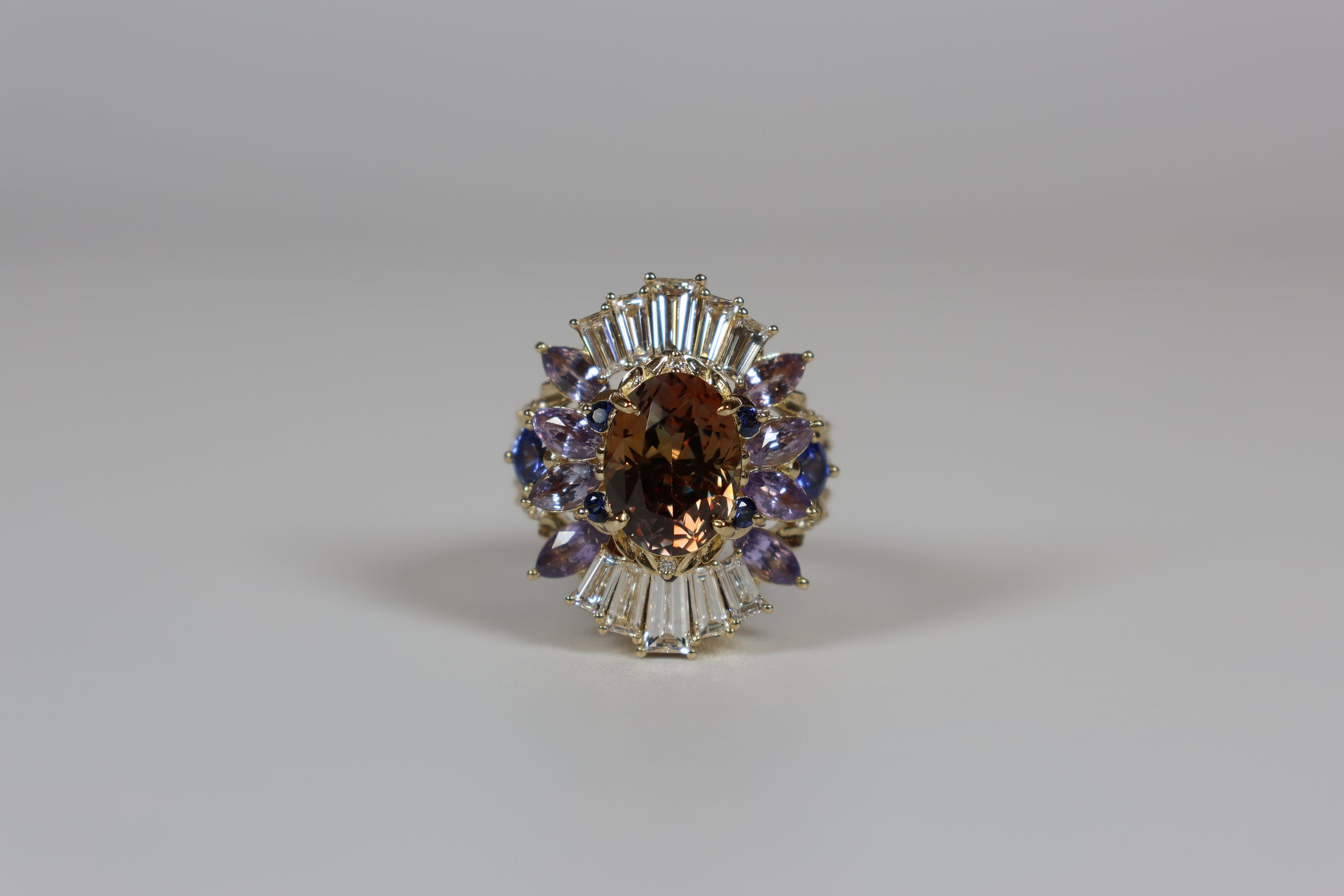 Jewelry ring with a large central oval brown gemstone, surrounded by purple and clear stones in a decorative setting.