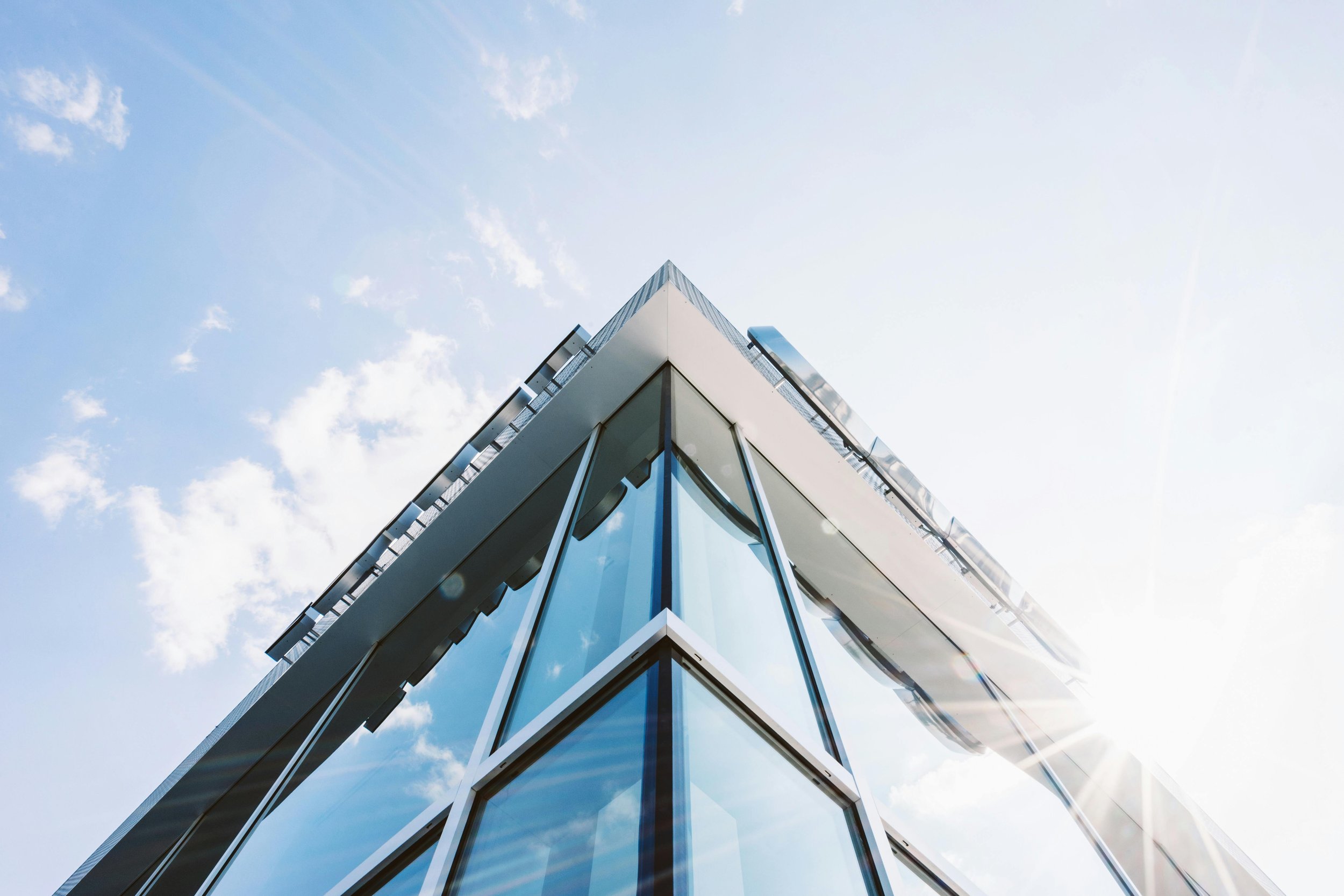 Modern glass building corner against a blue sky with clouds and sunlight.