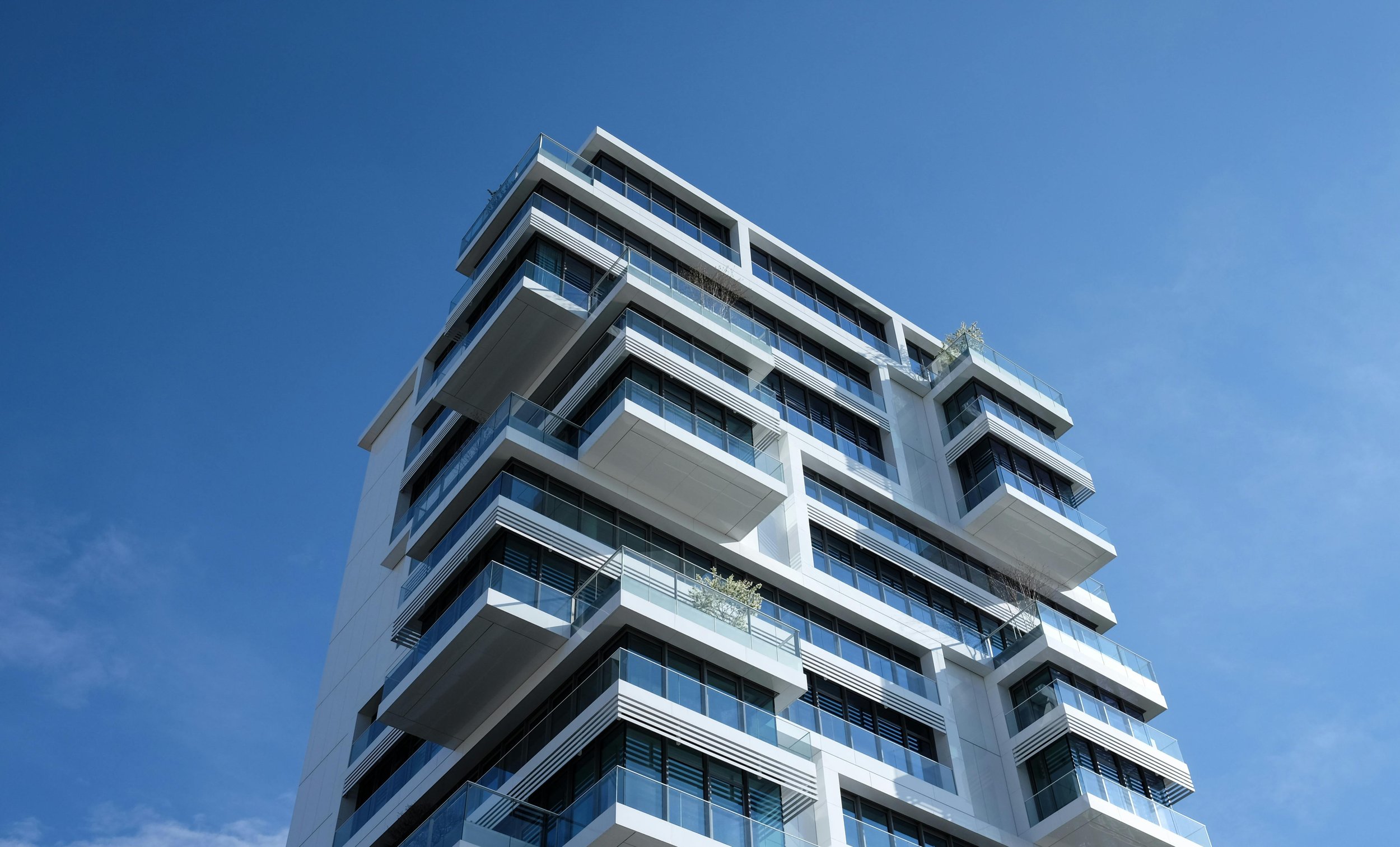 Modern high-rise building with glass balconies against a clear blue sky.