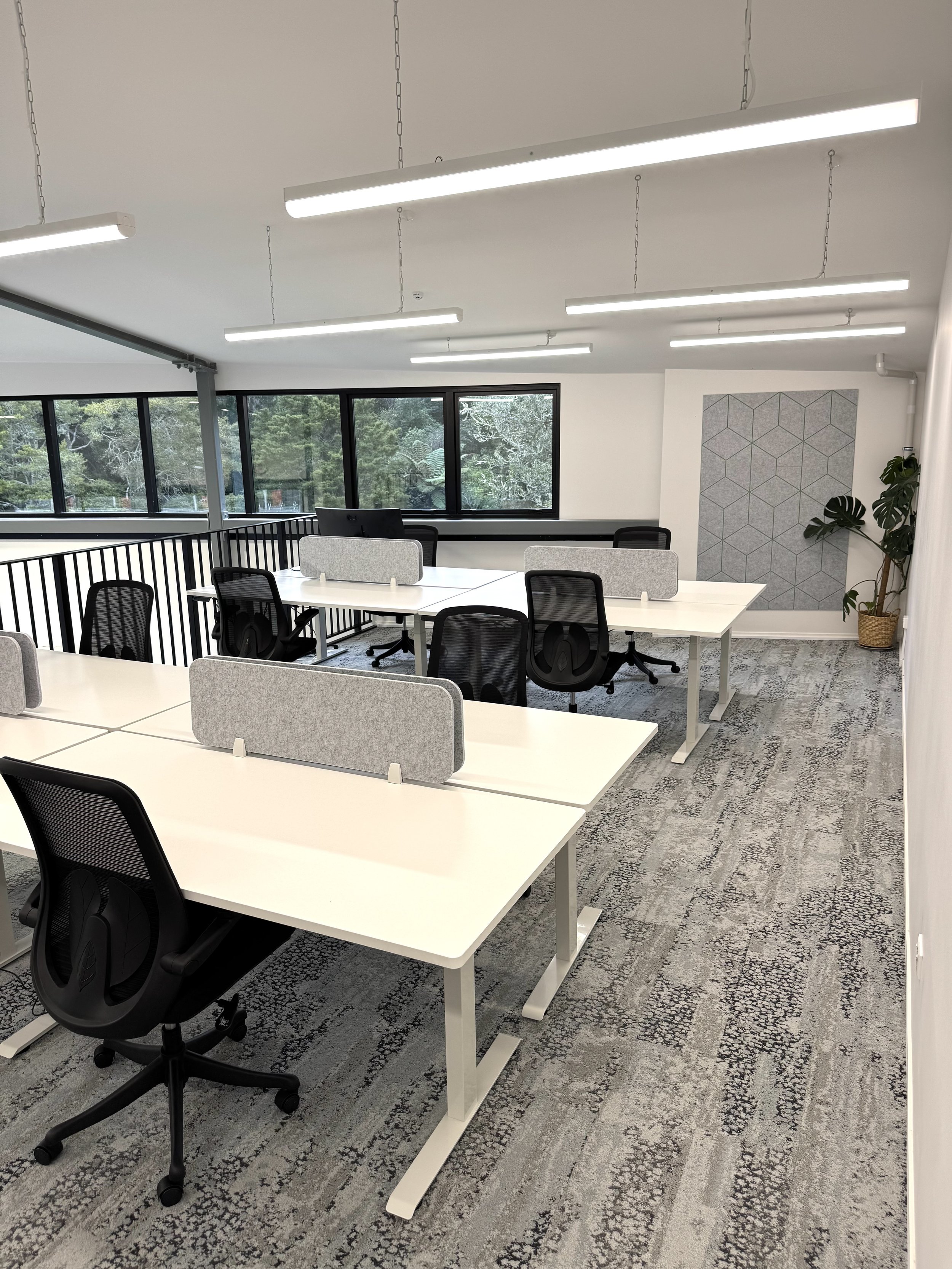 Modern office conference room with a white table, green velvet chairs, a laptop, a coffee mug, a green glass, and a large window with a view of trees and neighboring houses.