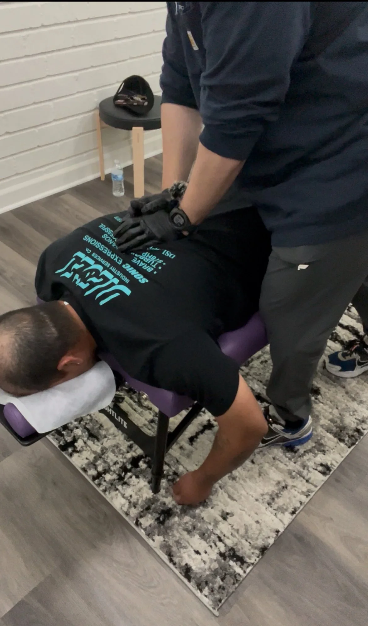 A person receiving a massage or chiropractic treatment on their back while lying face down on a massage table, with their head resting on a pillow.