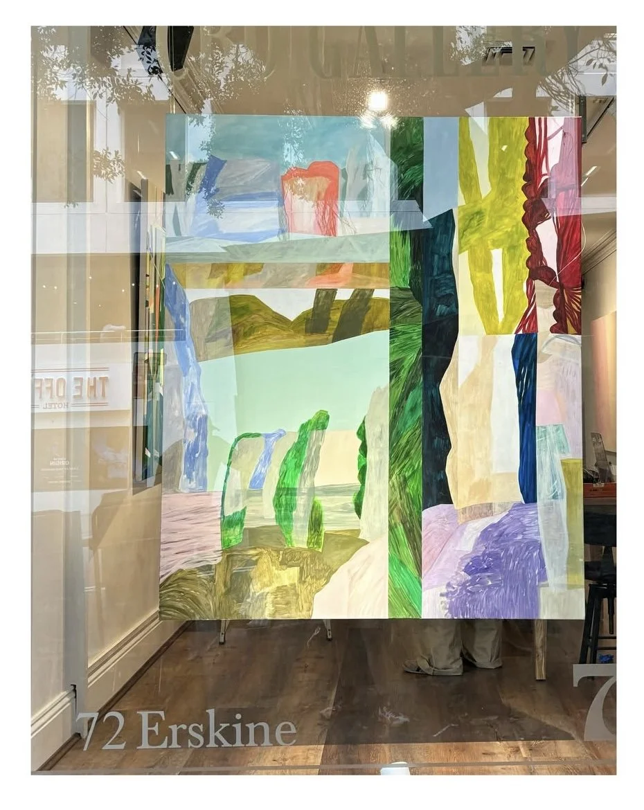 Colorful abstract painting on glass, featuring various shapes and colors including green, blue, red, yellow, black, and purple, with reflections of surroundings visible.