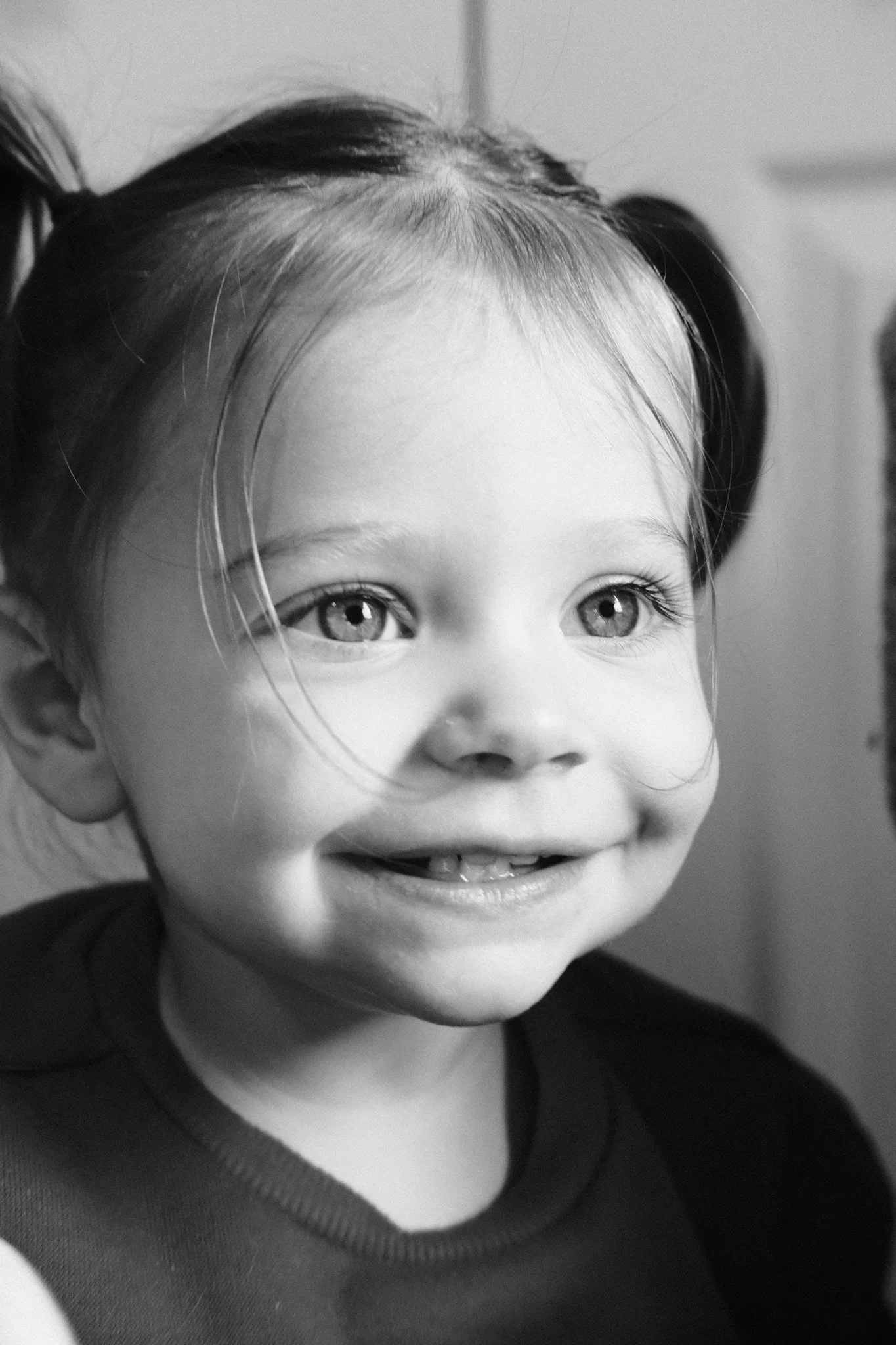 Close-up of a young girl with light-colored eyes, smiling, with her hair in pigtails, in black and white.
