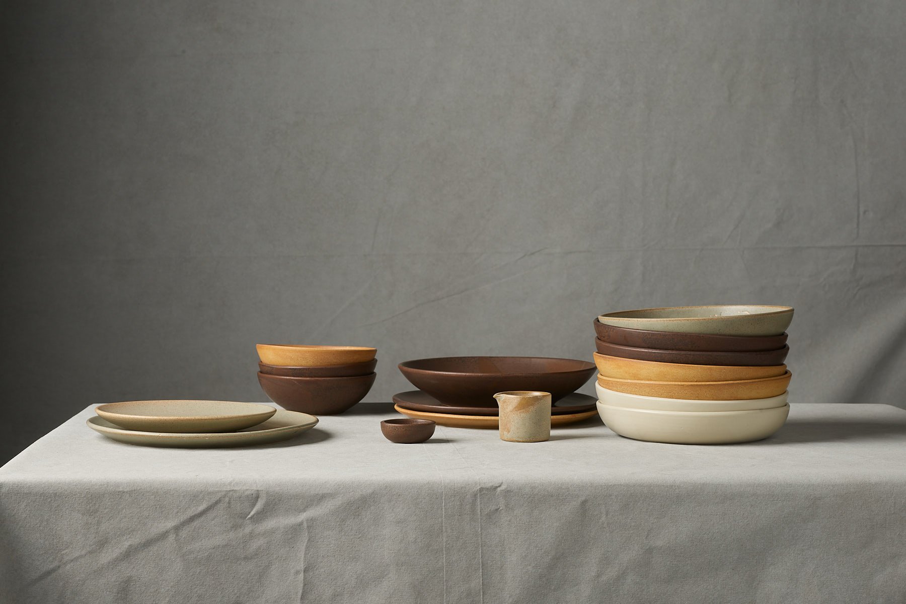 A collection of ceramic bowls and plates on a white tablecloth with a plain gray background.