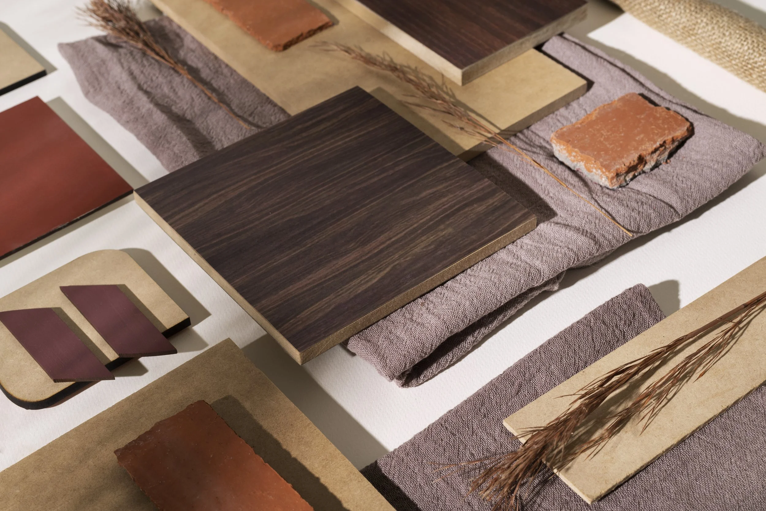 Sample display of various wood, tile, and stone materials arranged on fabric and paper, including dark and reddish-brown wood panels, tiles, and brick pieces.