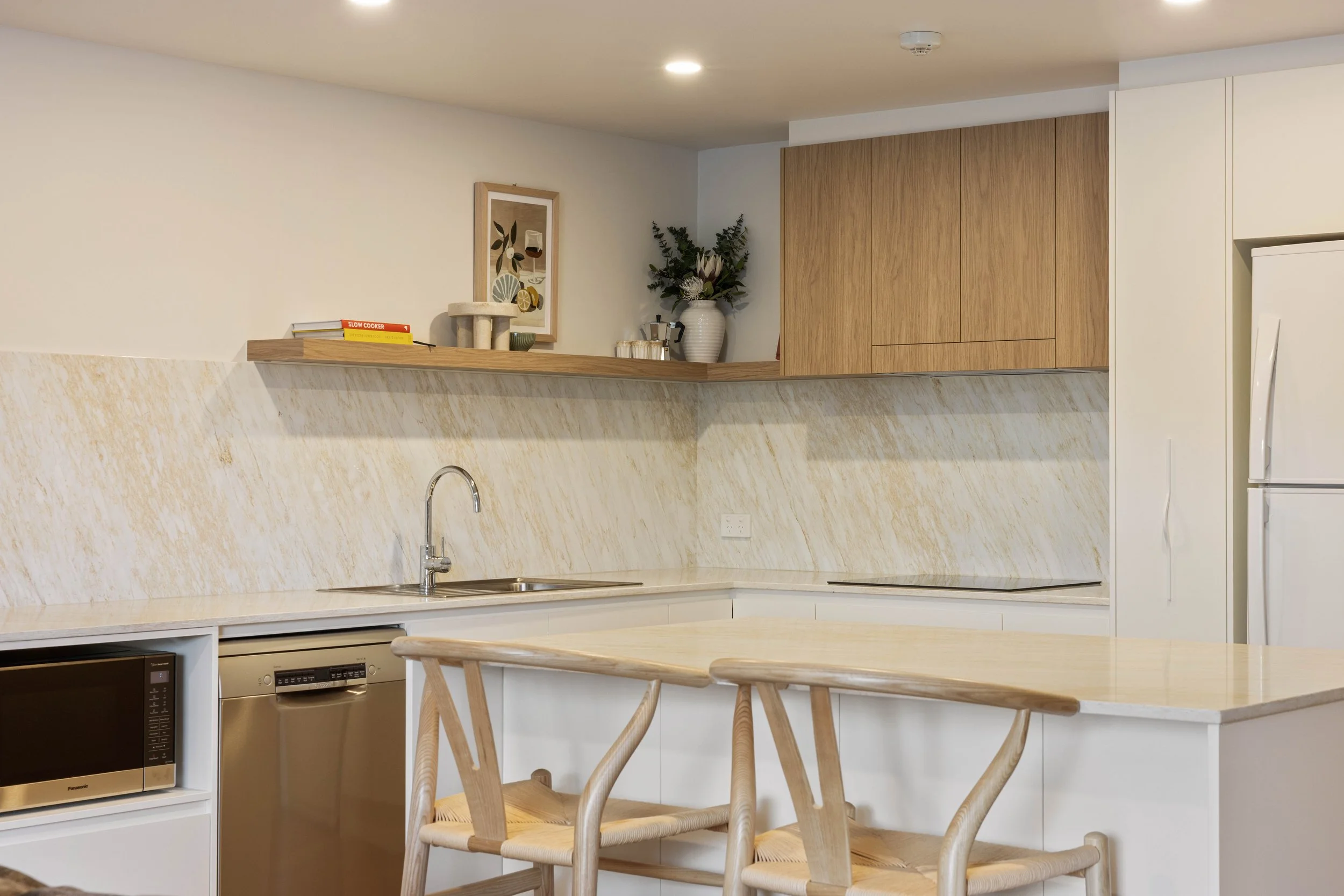 Warm, neutral Kitchen using Laminex White cabinets and timber overheads. Stone benchtops and splashback creating a clean, bright and open space. 