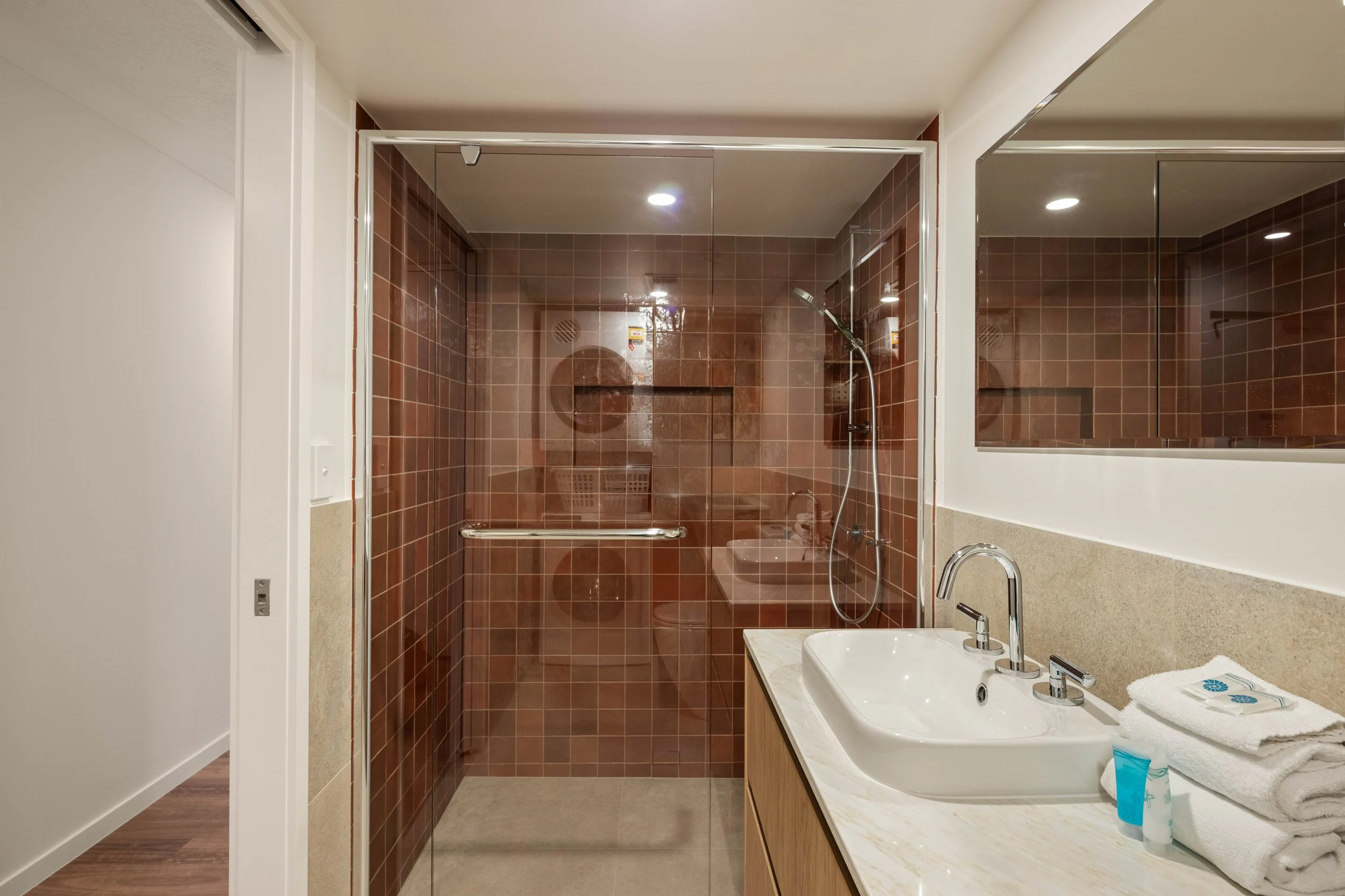 Deep terracotta tiles to shower paired with timber joinery, stone benchtops and neutral tiles throughout the Bathroom and Laundry. 