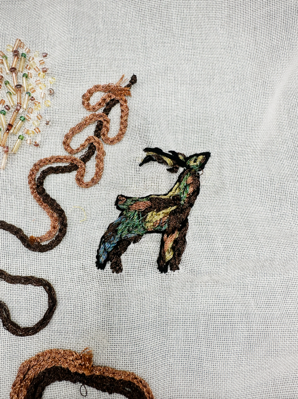 Broderie de cerf colorée sur tissu à mailles avec fils et perles.
