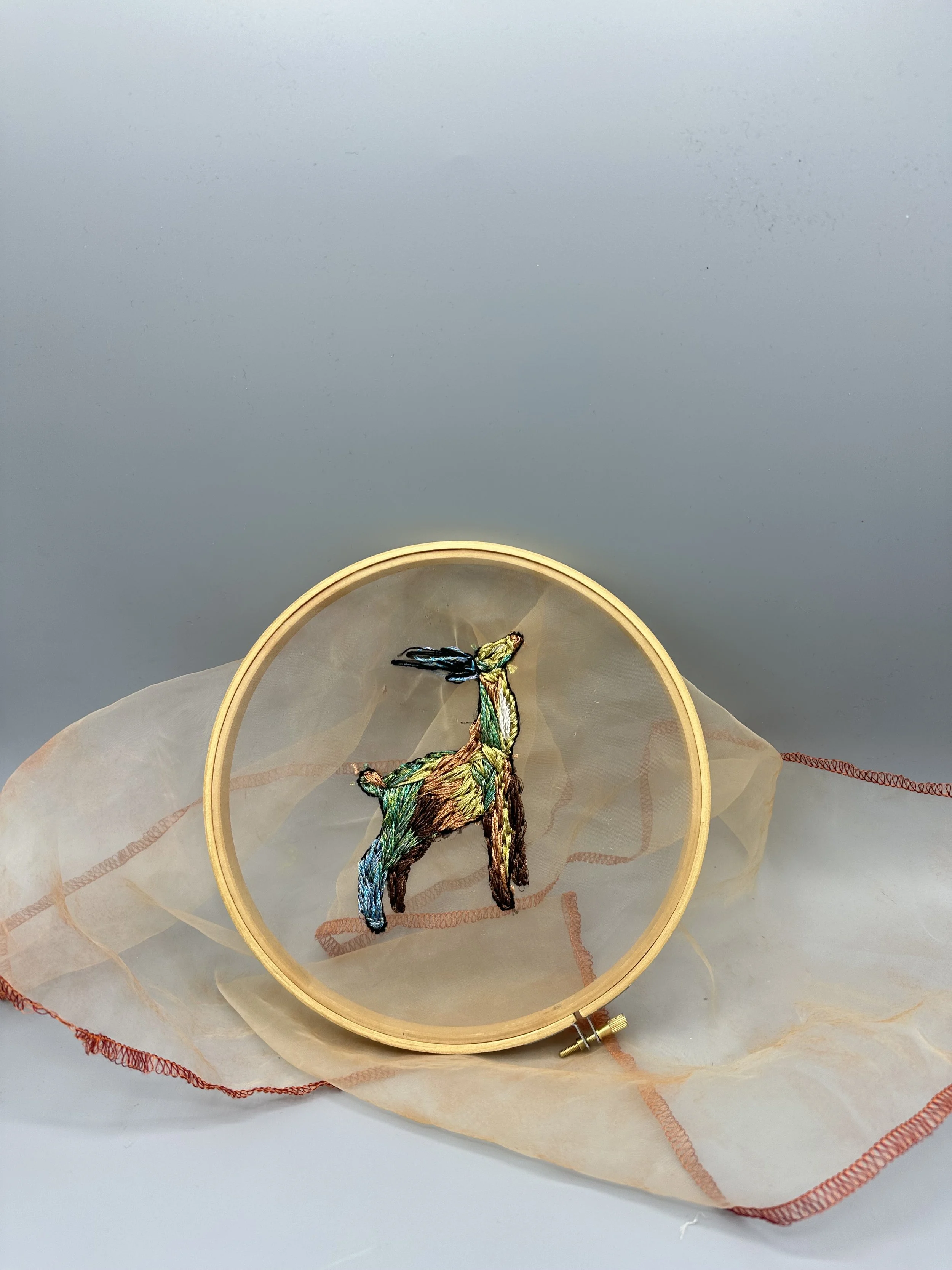 Broderie d'un animal dans un cercle à broder en bois, posé sur un tissu transparent beige avec des bords orange.