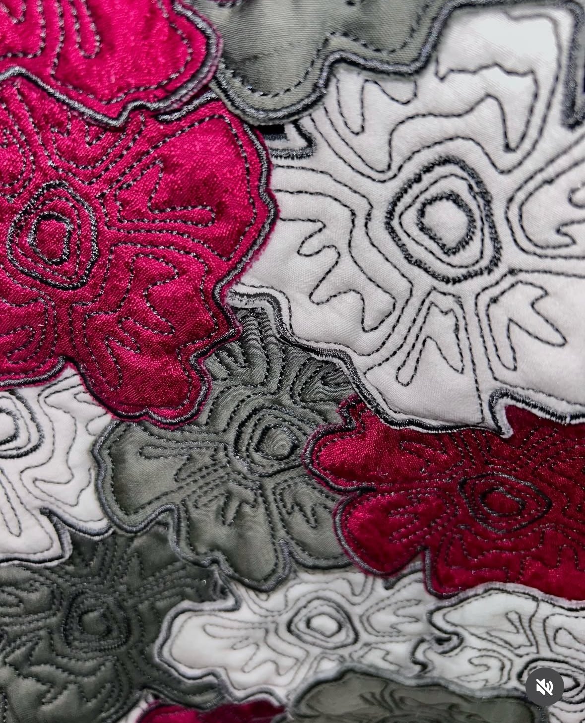 Motif floral brodé avec des fleurs rouges et grises sur un tissu blanc.