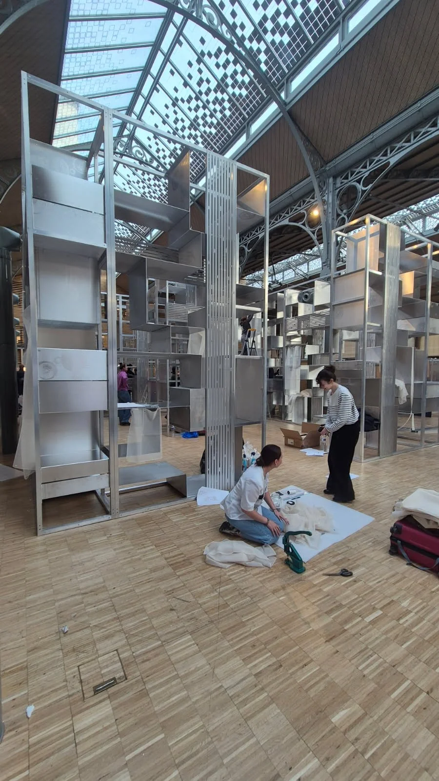 Femme portant un vêtement noir rembourré avec des motifs de triangles, et un tissu blanc à franges avec des inscriptions noires.