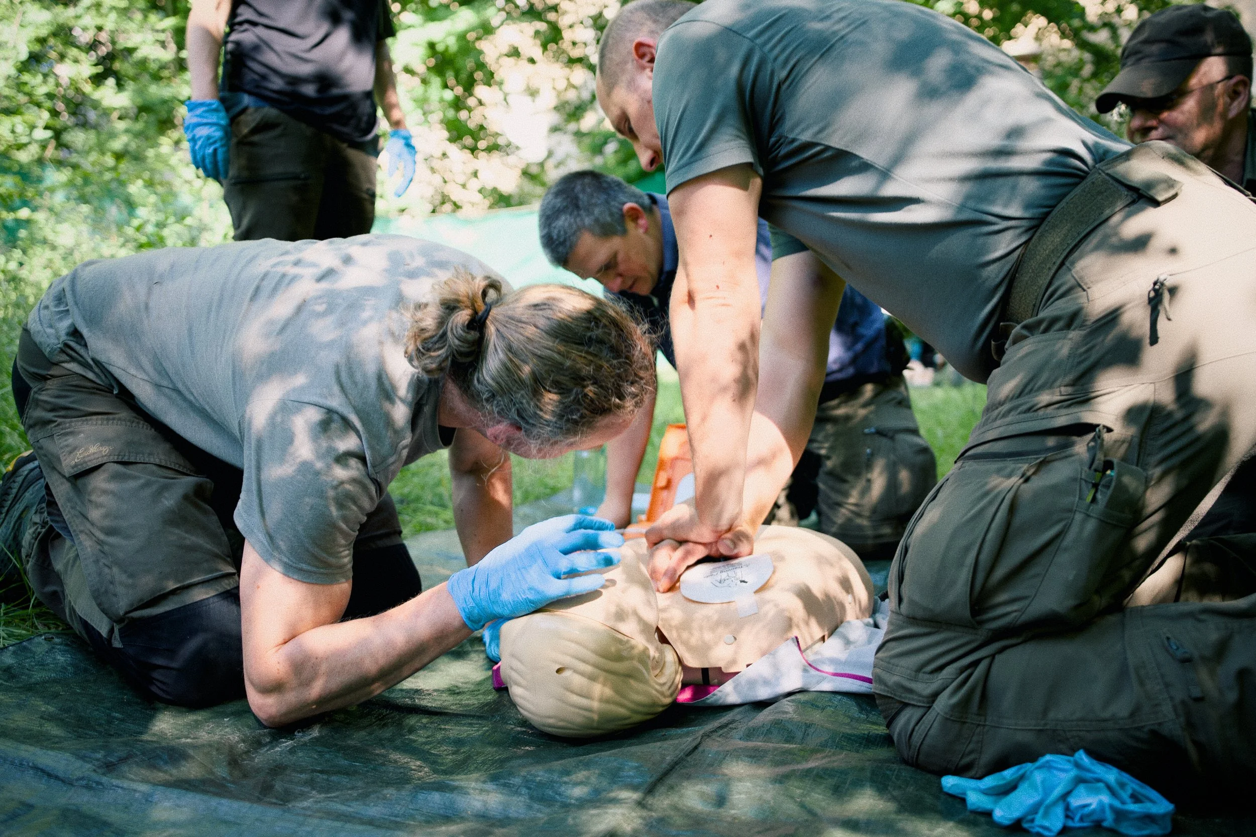 Menschen üben Erste-Hilfe an einer Übungspuppe draußen im Gelände, um die Herz-Lungen-Wiederbelebung zu lernen.