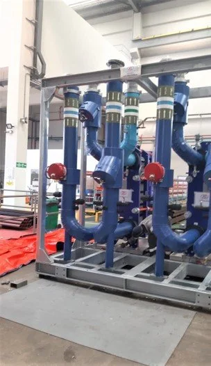 Industrial piping system with large blue pipes, red valves, and metal support framework in a factory setting.