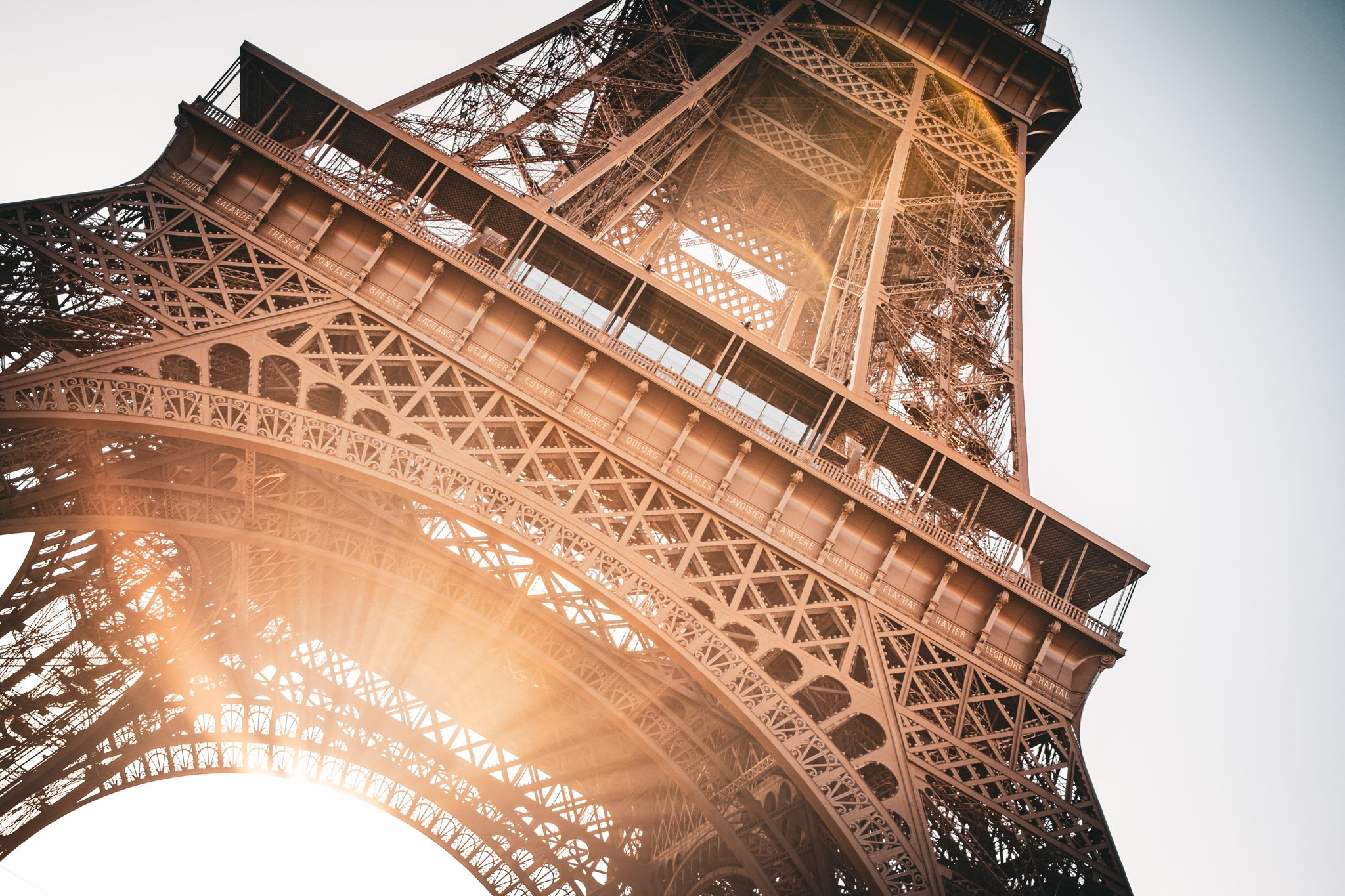 Close-up view of the Eiffel Tower structure with sunlight filtering through its iron lattice.
