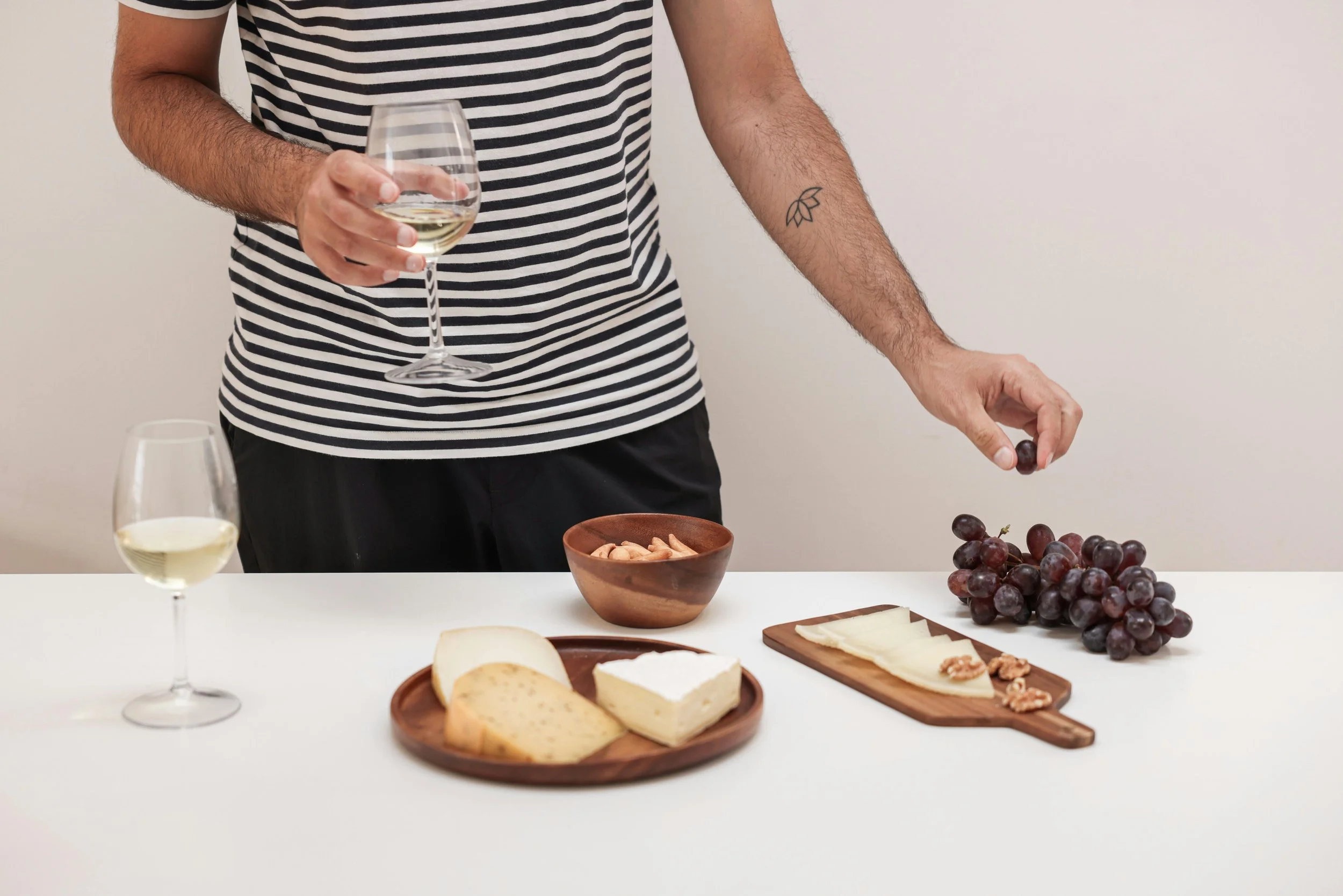 Person holding wine glass with cheese, breadsticks, grapes, and nuts on table