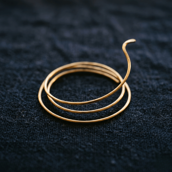 Close-up of a gold wire ring coiled in a spiral with a curved, elongated end, placed on dark fabric. Pattern Rewiring