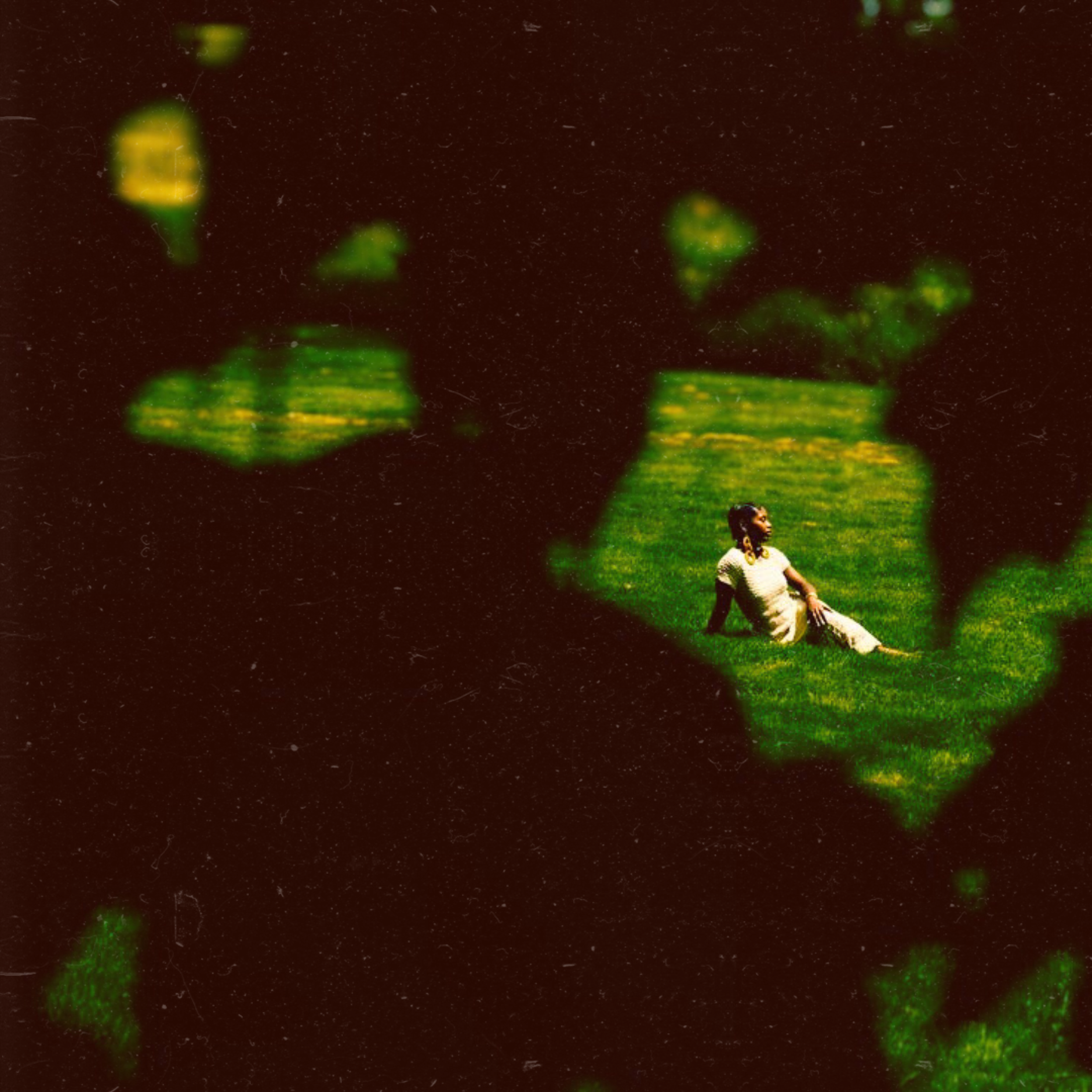 A person sitting on the grass, surrounded by the green silhouettes of two hands forming a heart shape, with a dark background.