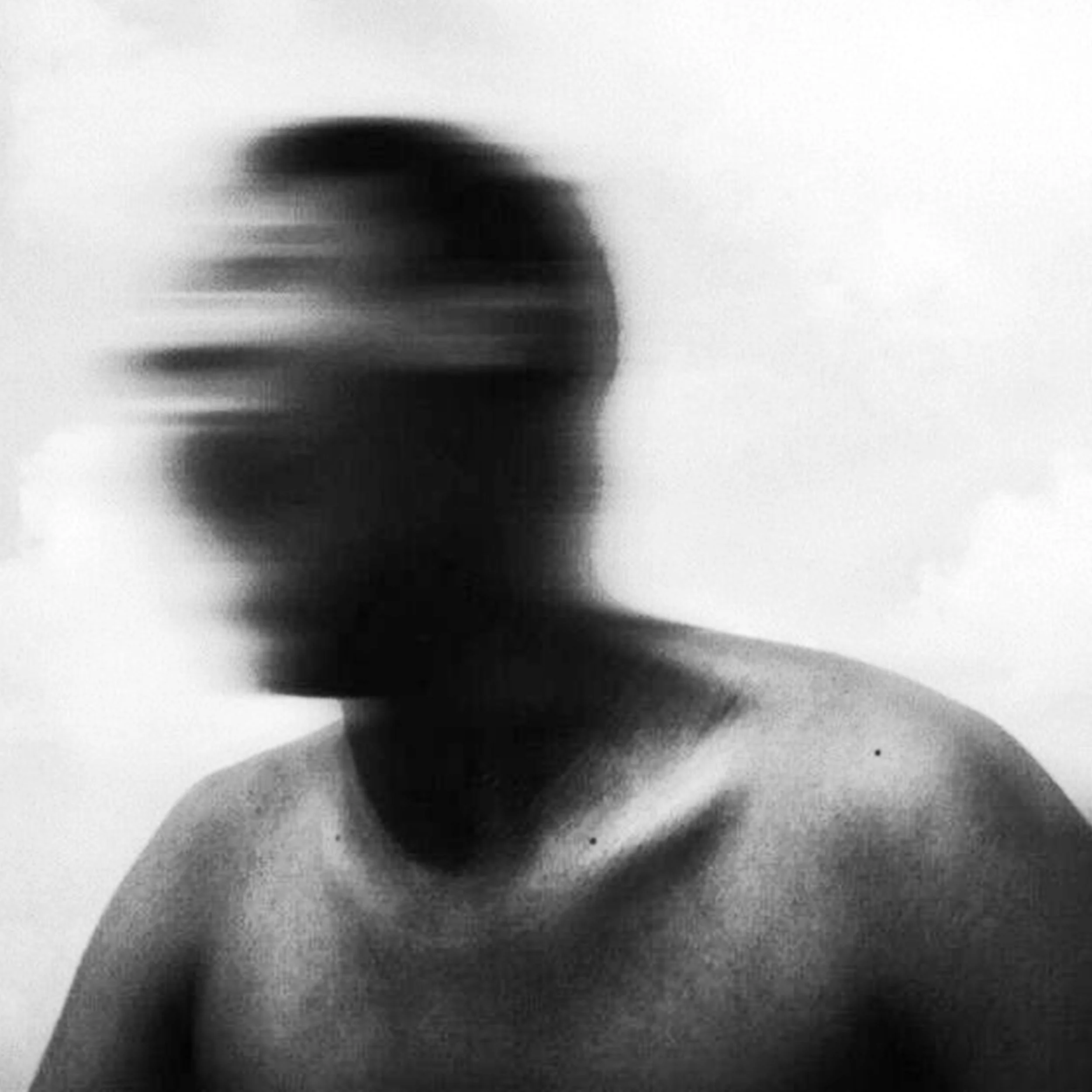 Black and white photo of a shirtless person with blurred face and hair, facing slightly to the right.