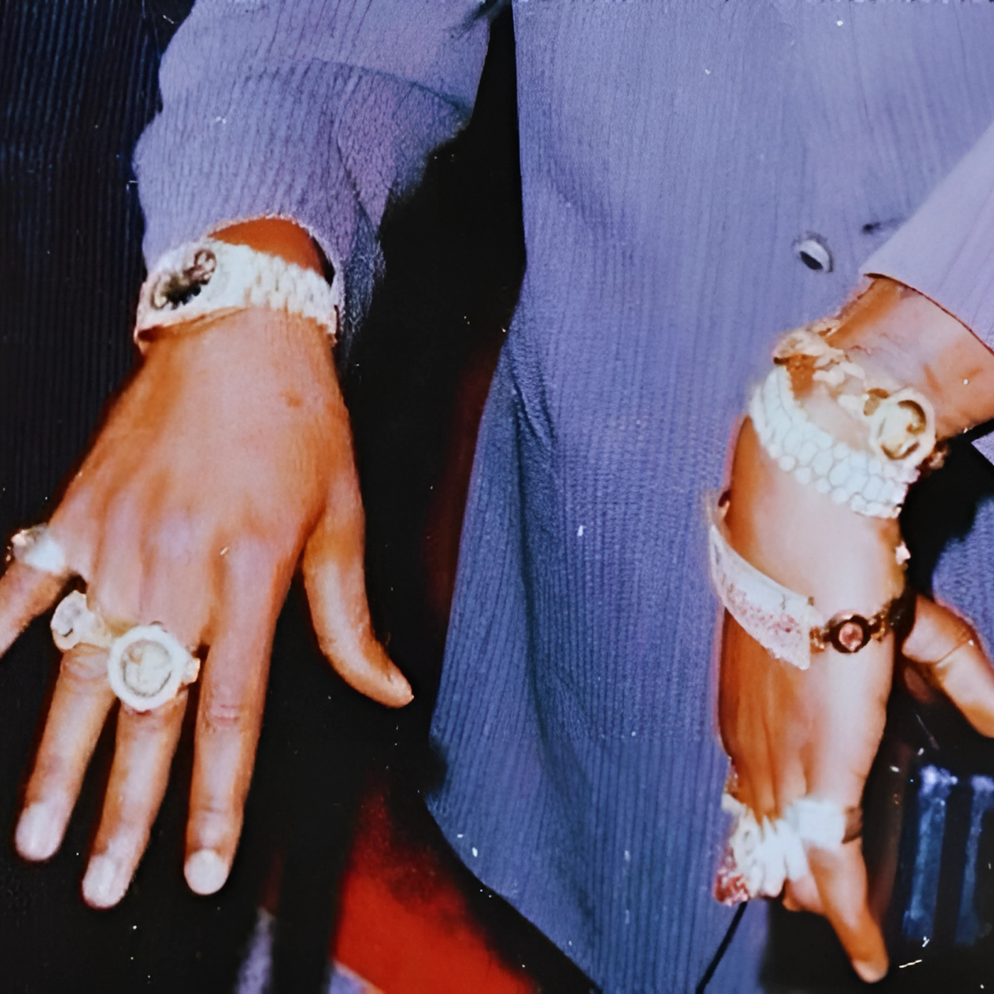 Close-up of a person's hands wearing multiple rings and bracelets, dressed in a gray blazer, with no visible face.