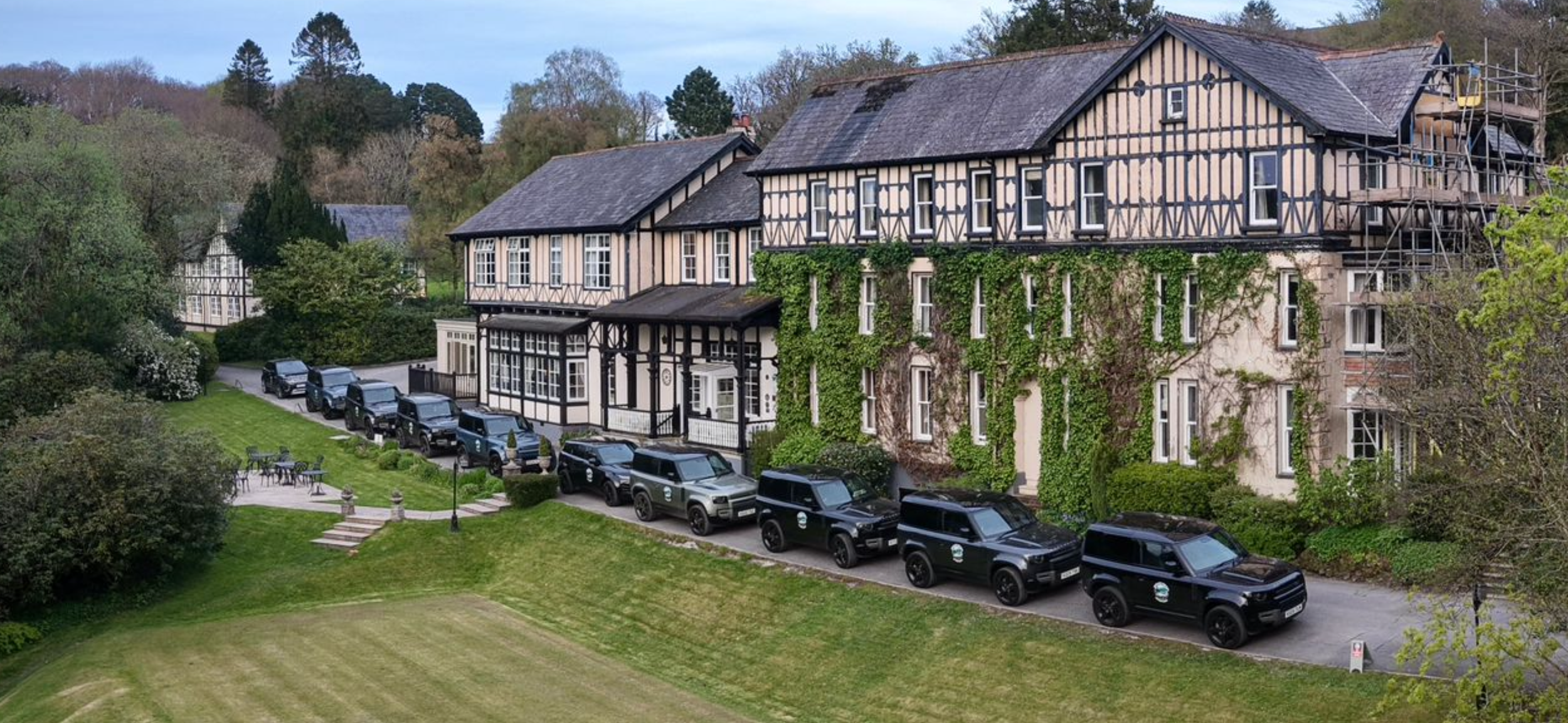  a line of land rover defenders in front of a country house hotel 