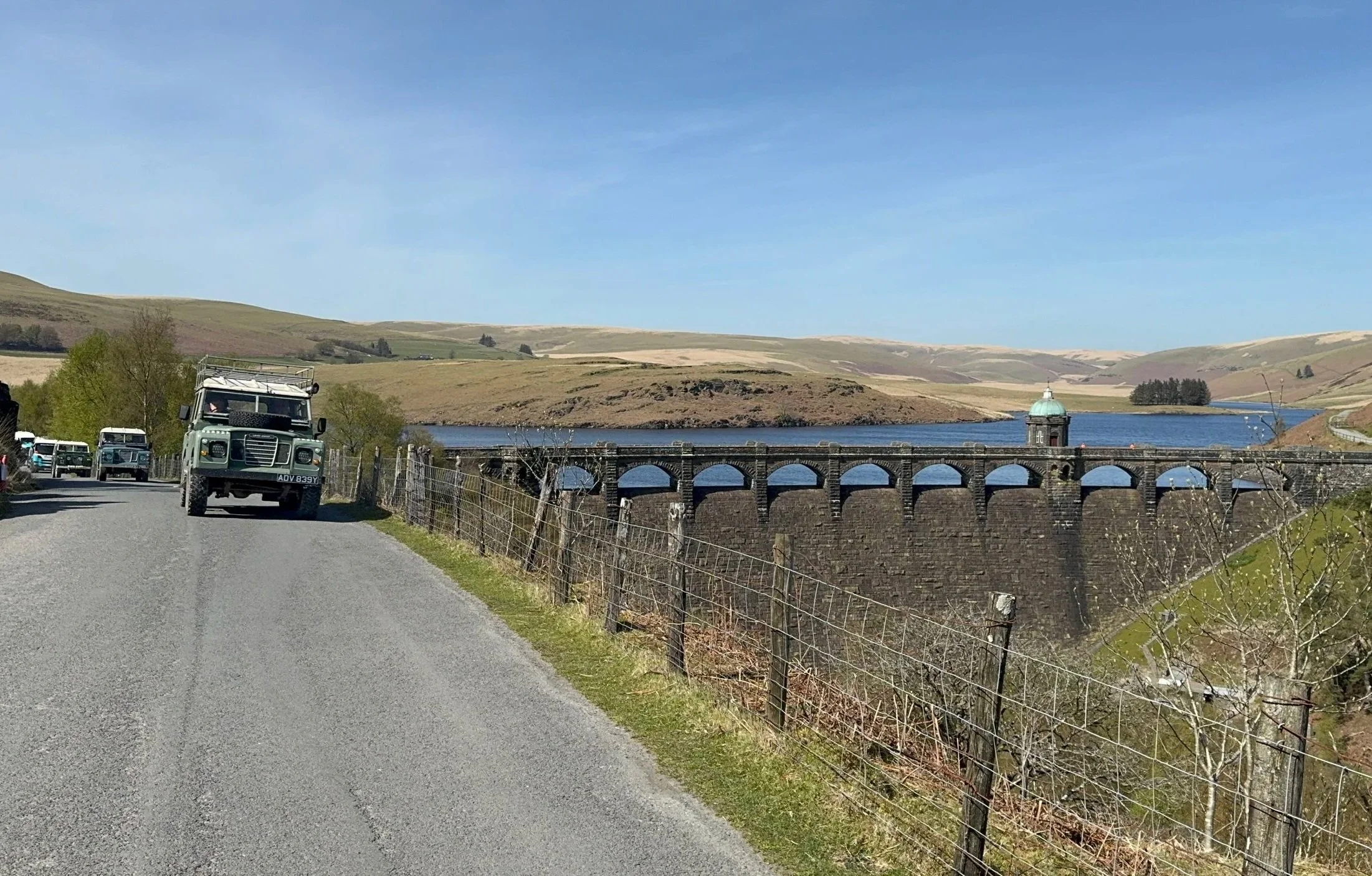  classic land rover driving along a dam 