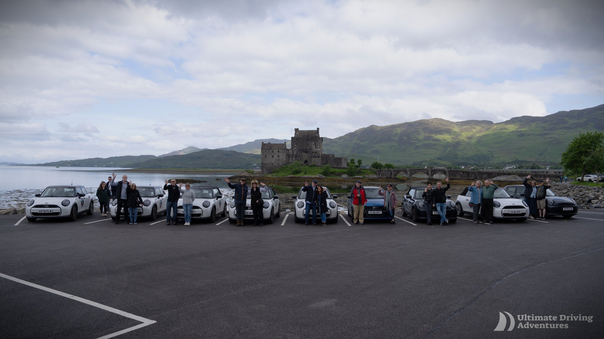 a line of Mini Coopers lined up in front of a castle names Eilean Donan Castle
