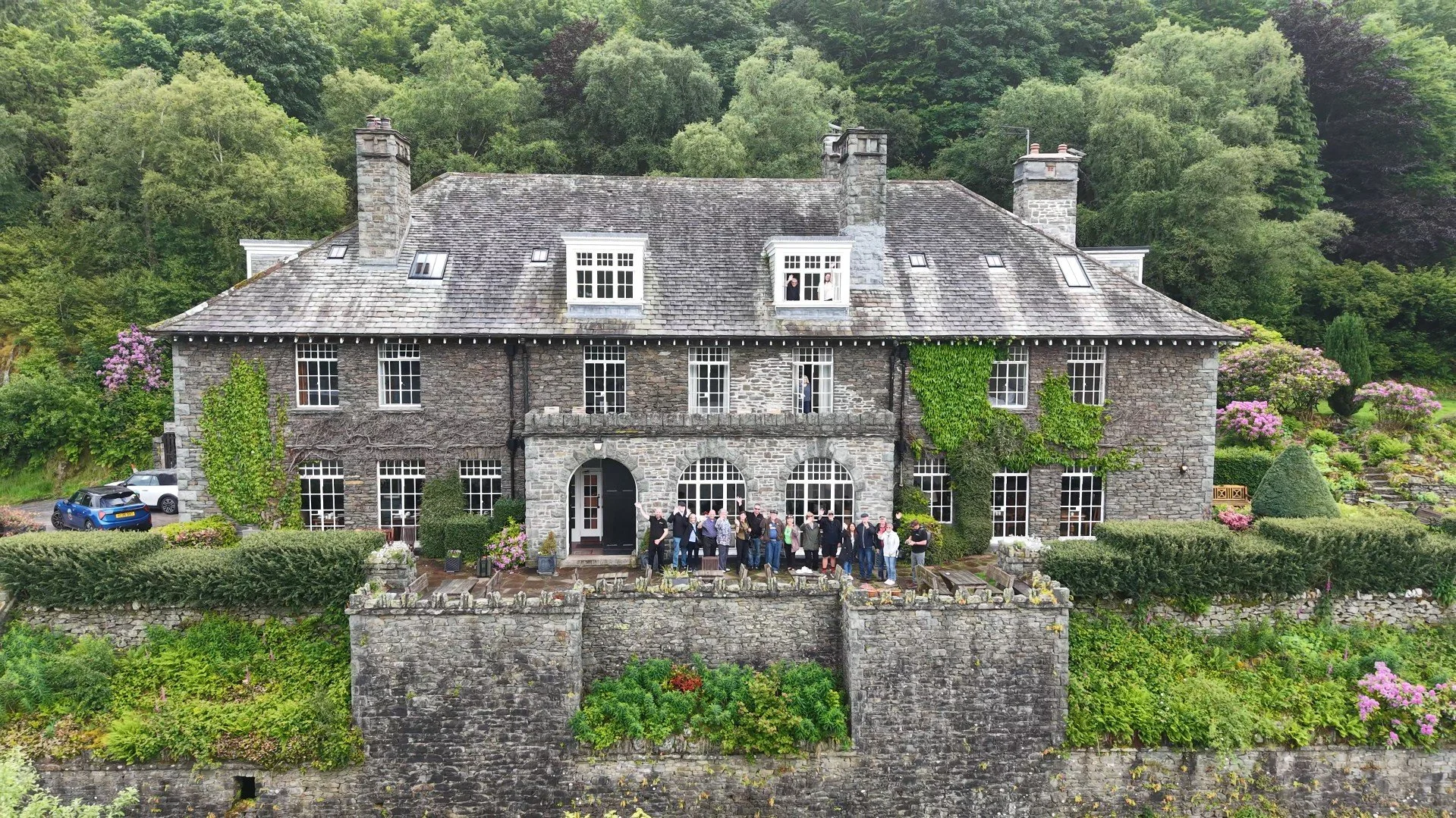 group of people waving with a grand hotel in the lake district behind them