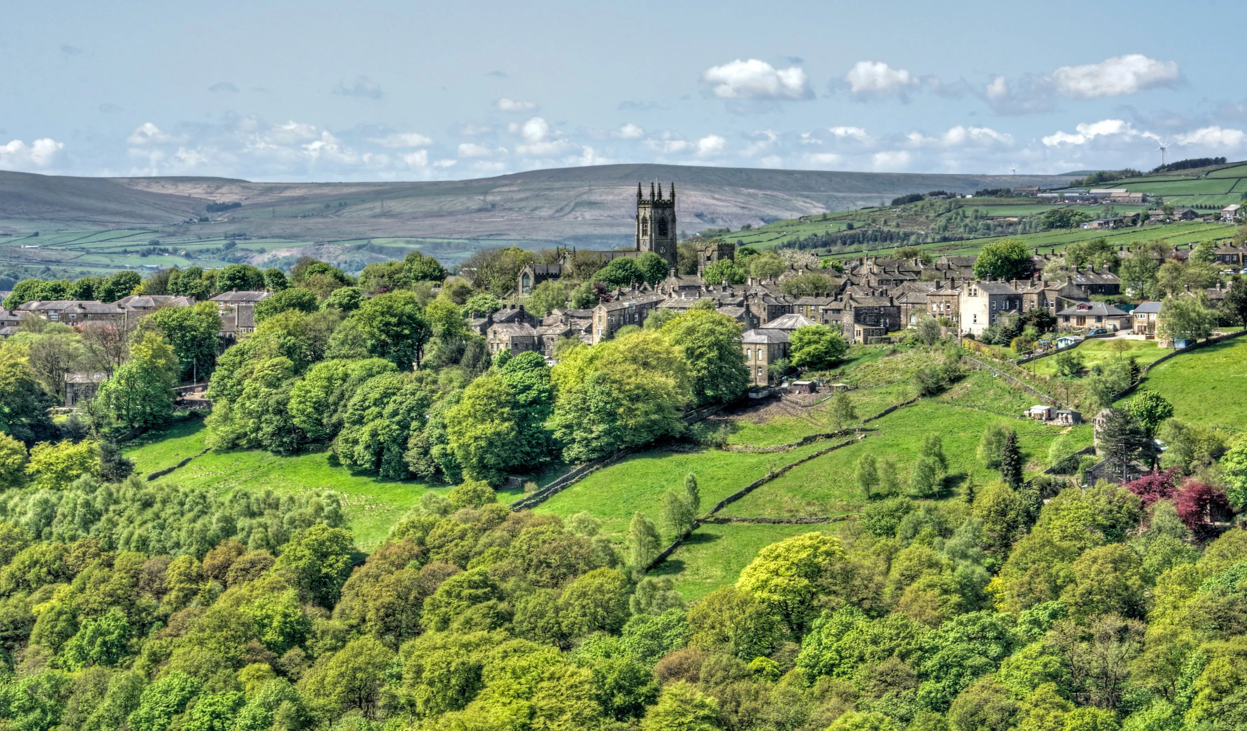 the pennine village of heptonstall viewed from across the calder valley with historic church houses and surrounding woodland and steep rocky hills