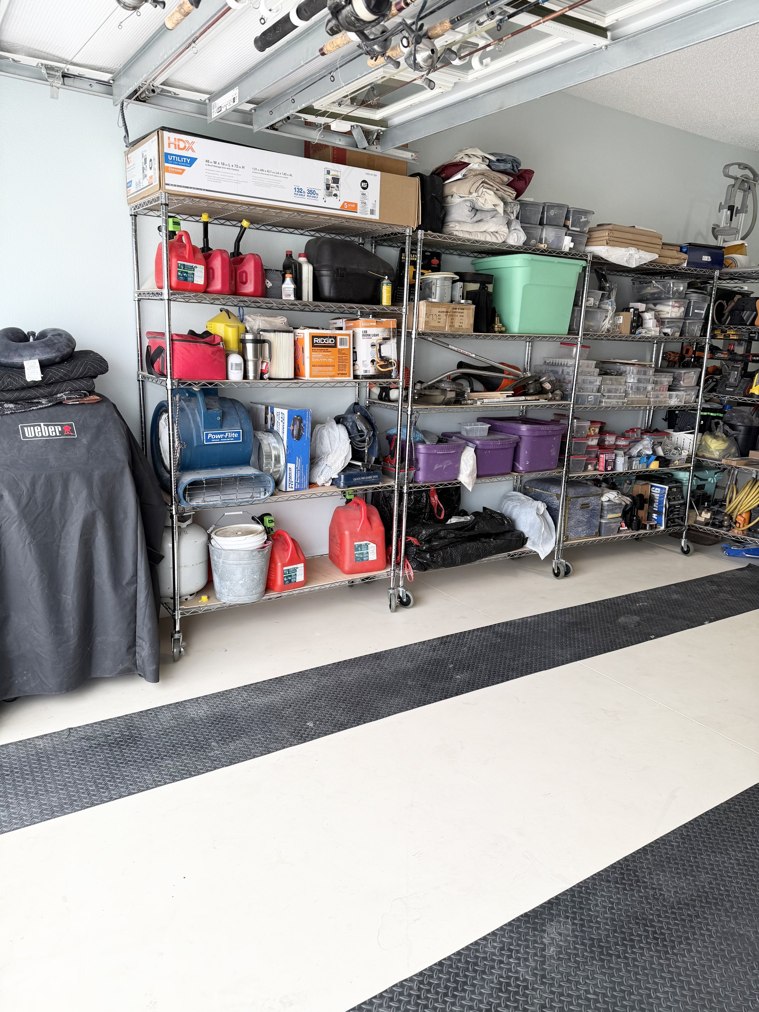 Organized garage with shelves containing tools, storage bins, and fuel containers.