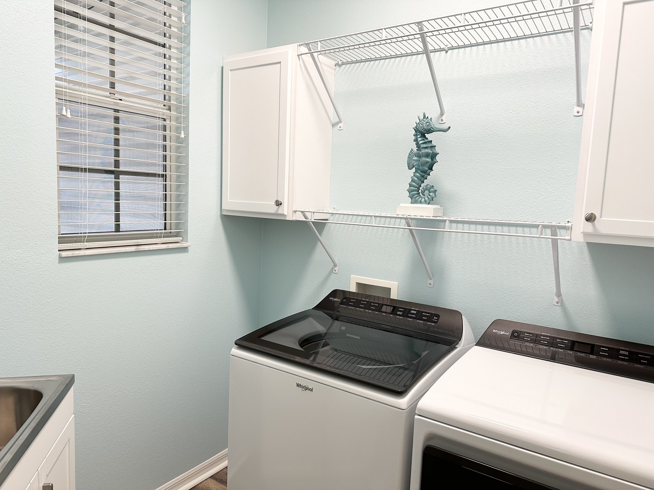 Laundry room with a window, washing machine, dryer, wall cabinets, and a decorative seahorse on a wire shelf.