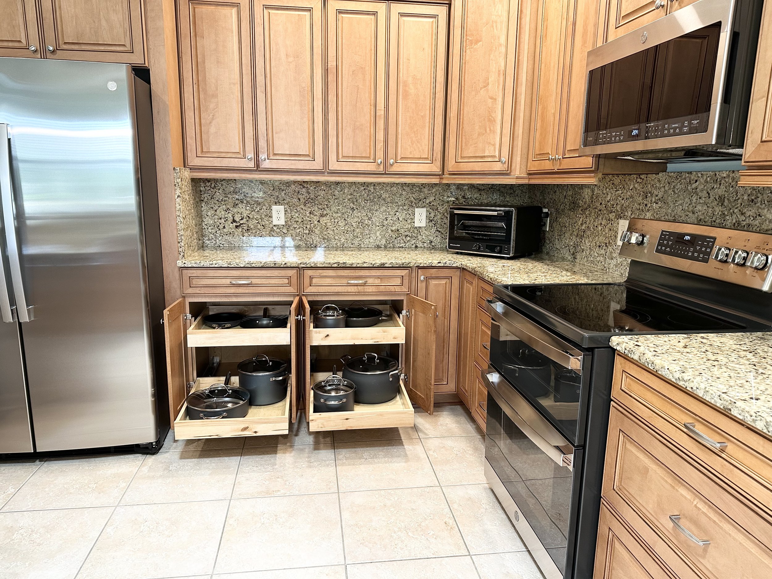 Modern kitchen with wooden cabinets, stainless steel appliances, open drawers with pots, granite countertops.